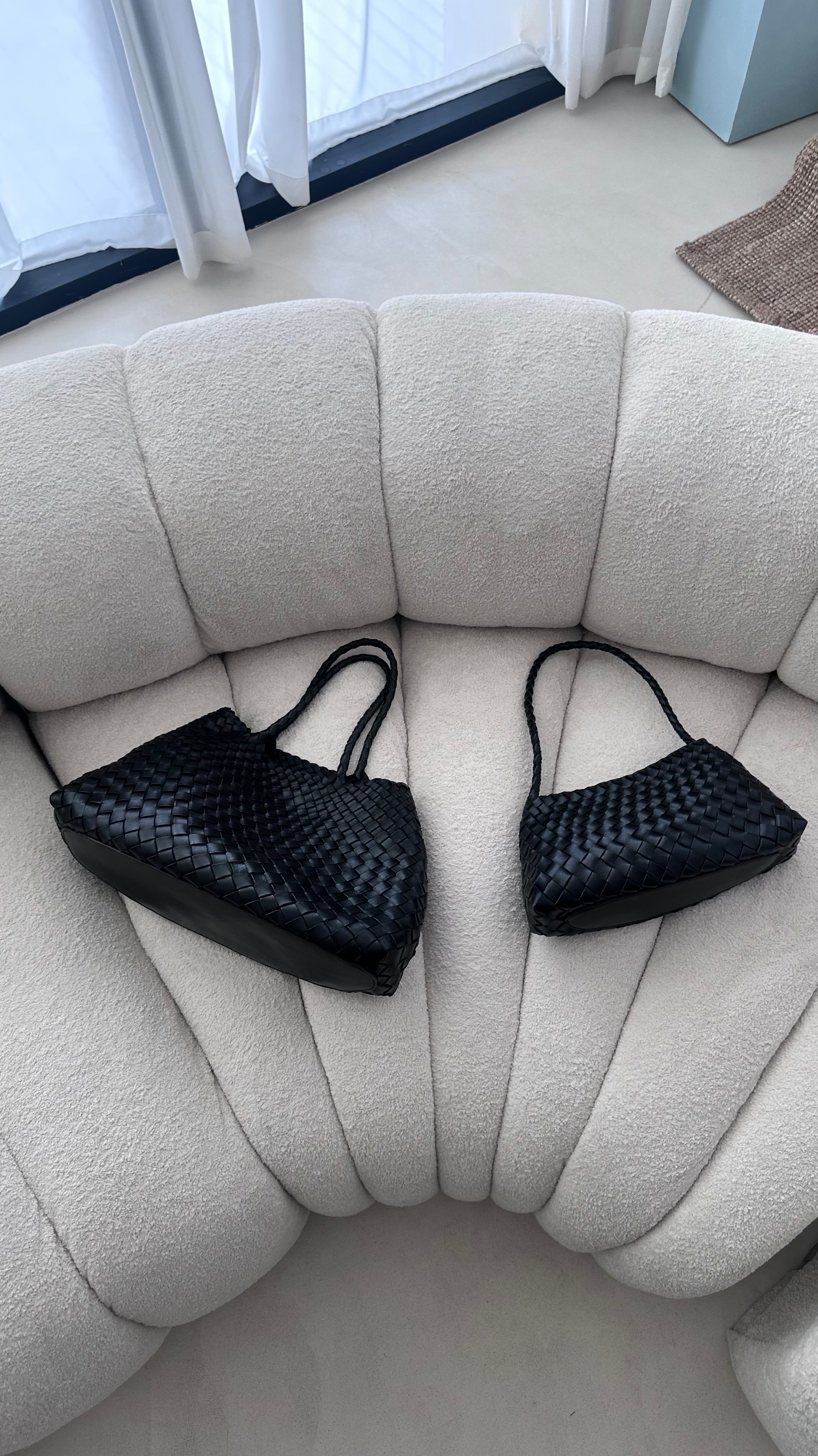 Two black woven handbags on a beige sofa.