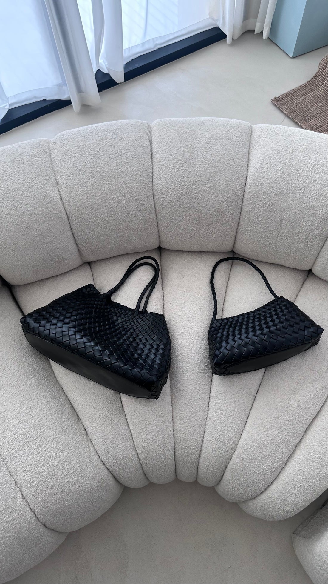 Two black woven handbags on a beige sofa.
