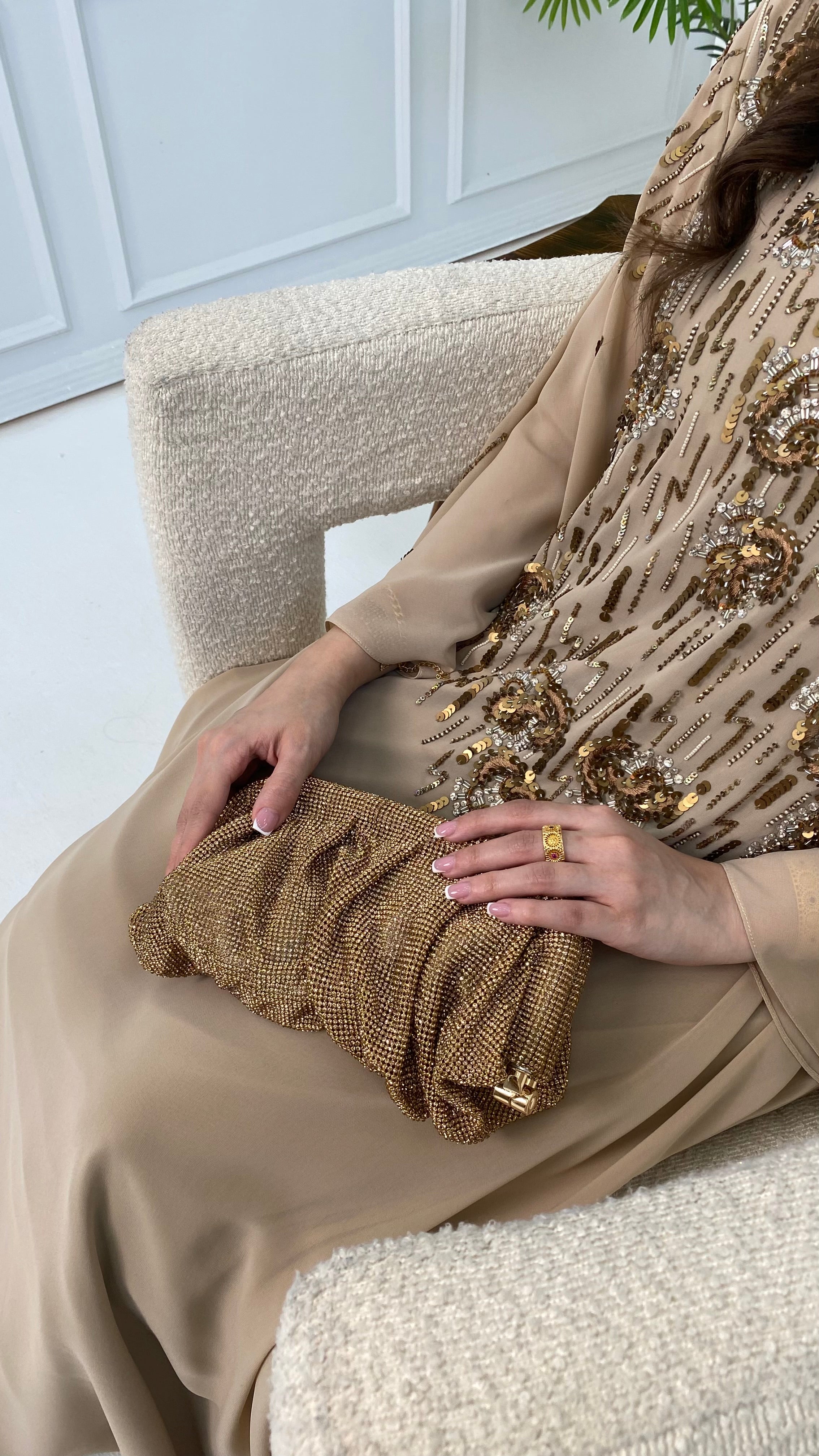 Person wearing a beige dress with a gold embellished shawl, sitting on a white chair.