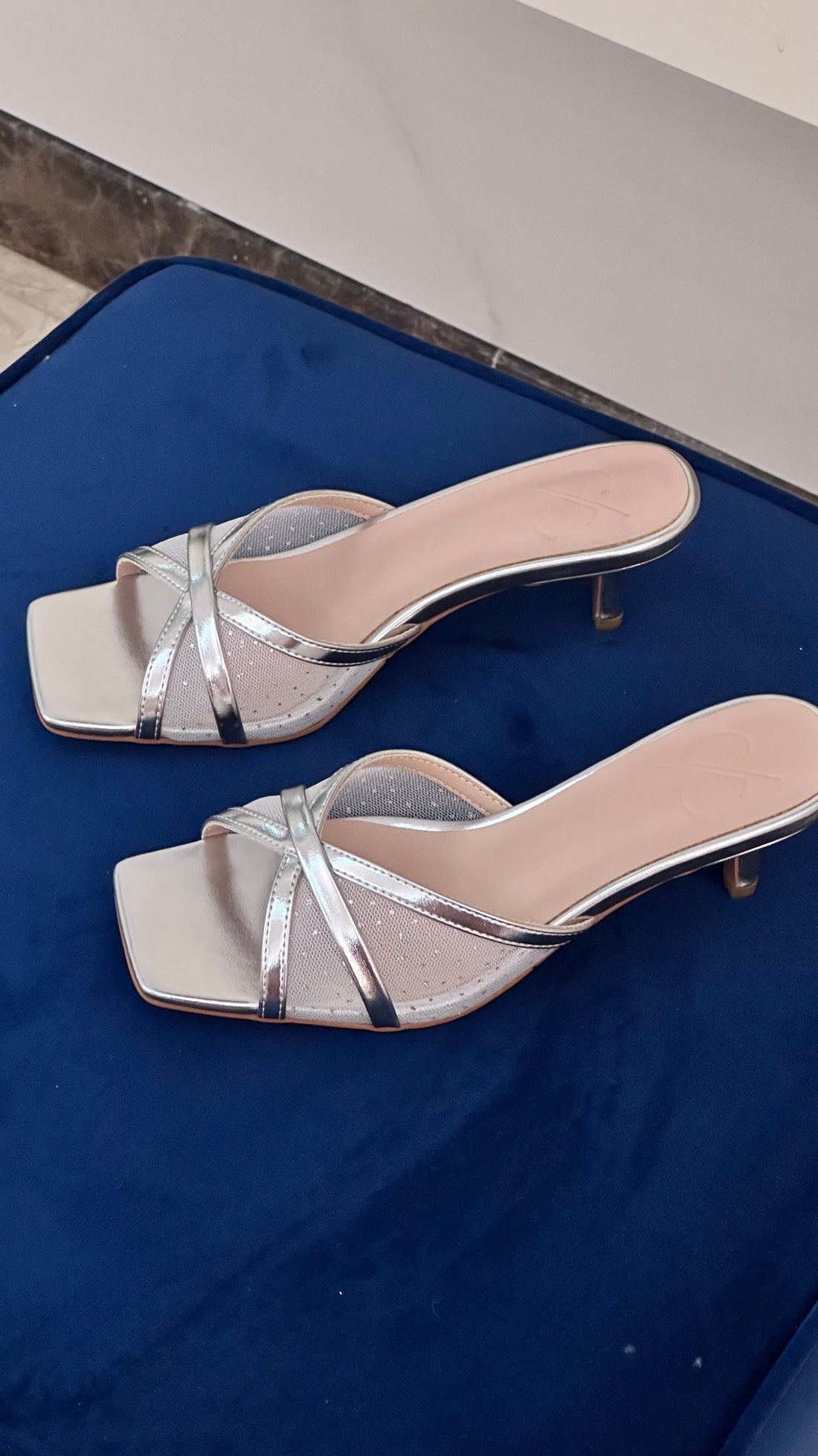 Silver high-heeled sandals on a blue surface