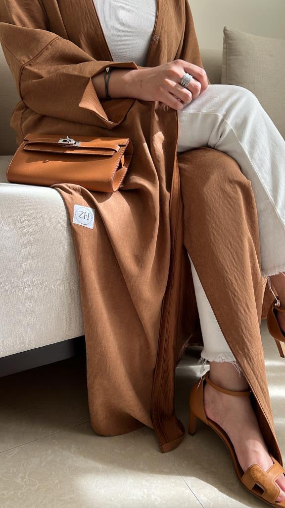 Person wearing a brown coat sitting on a couch with a matching handbag.