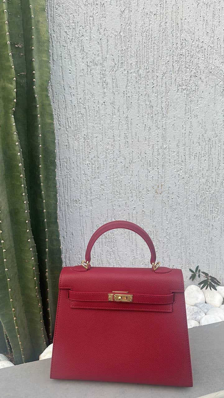 Red handbag with a gold clasp on a textured surface with a plant in the background