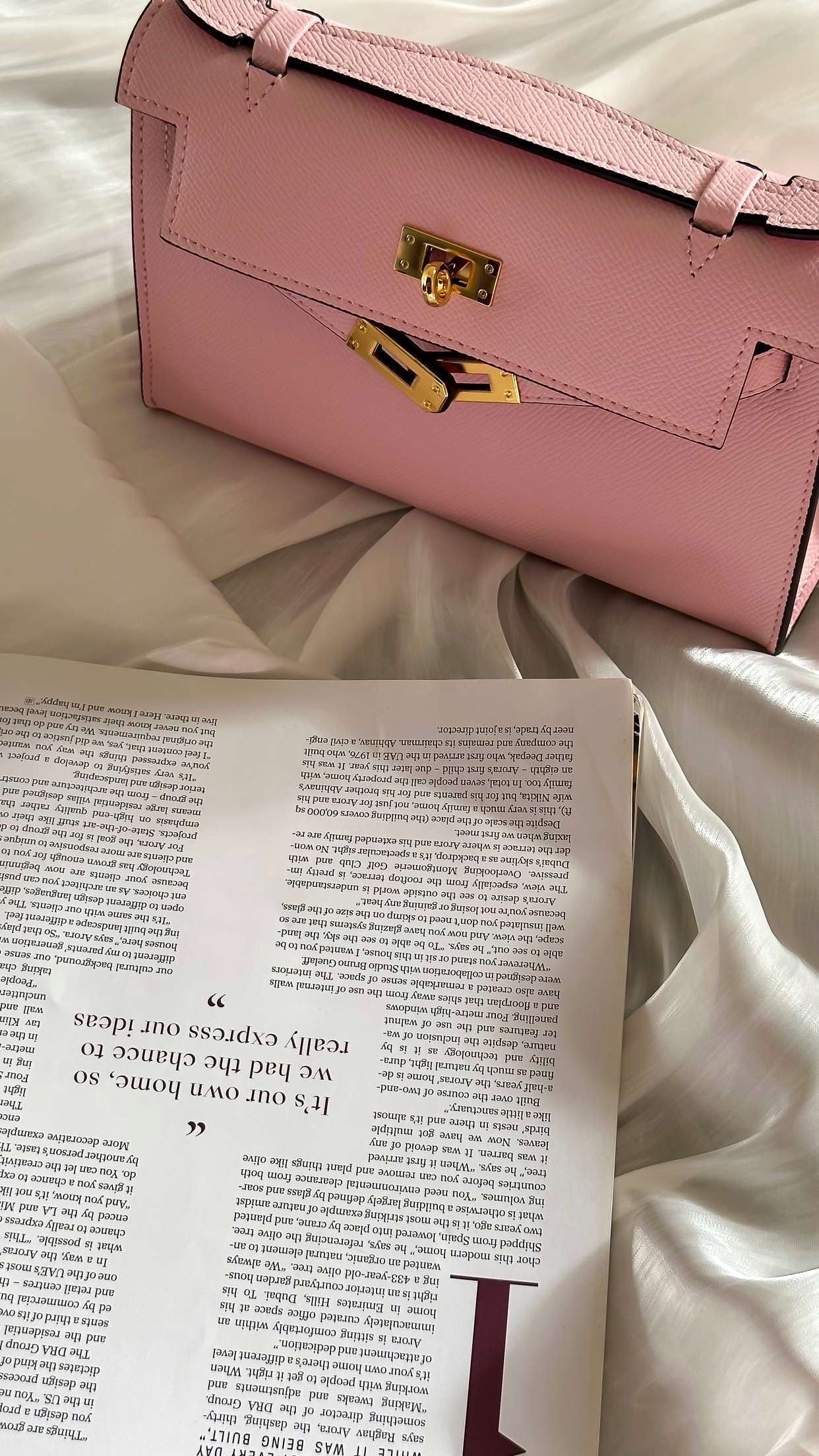 Pink handbag on a textured surface with an open magazine underneath