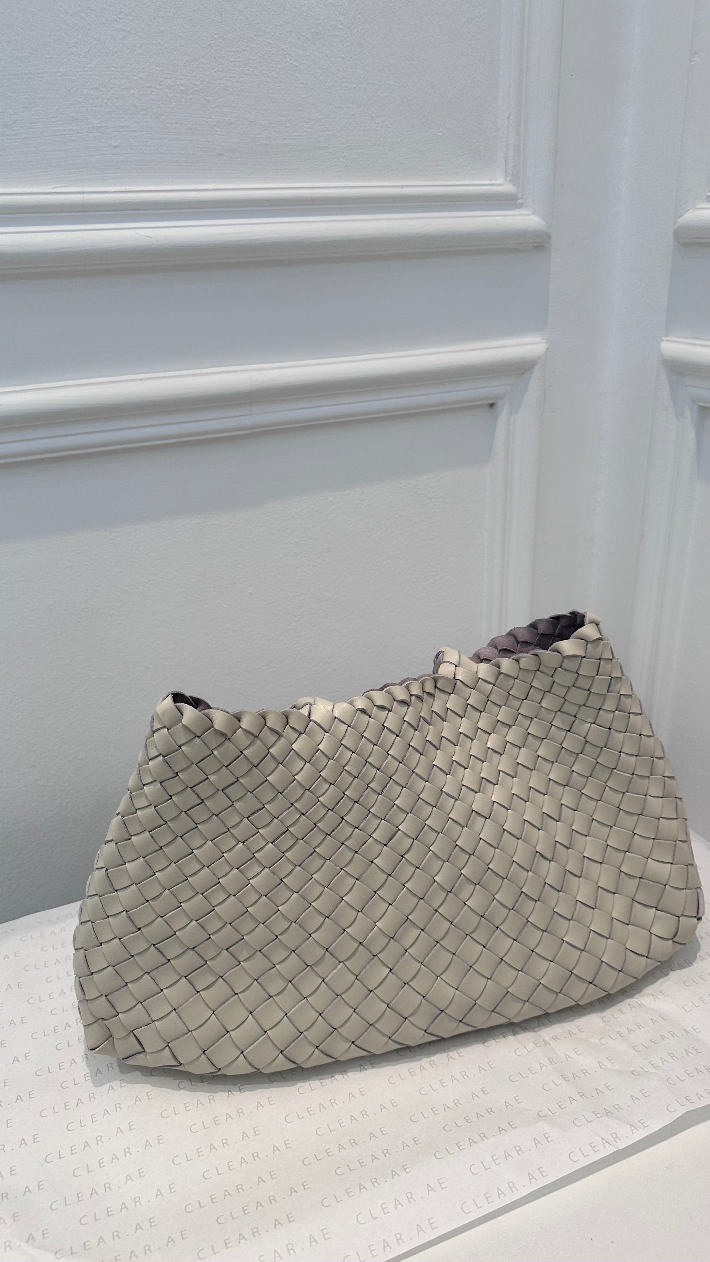 Woven handbag on a white surface with a light gray wall background