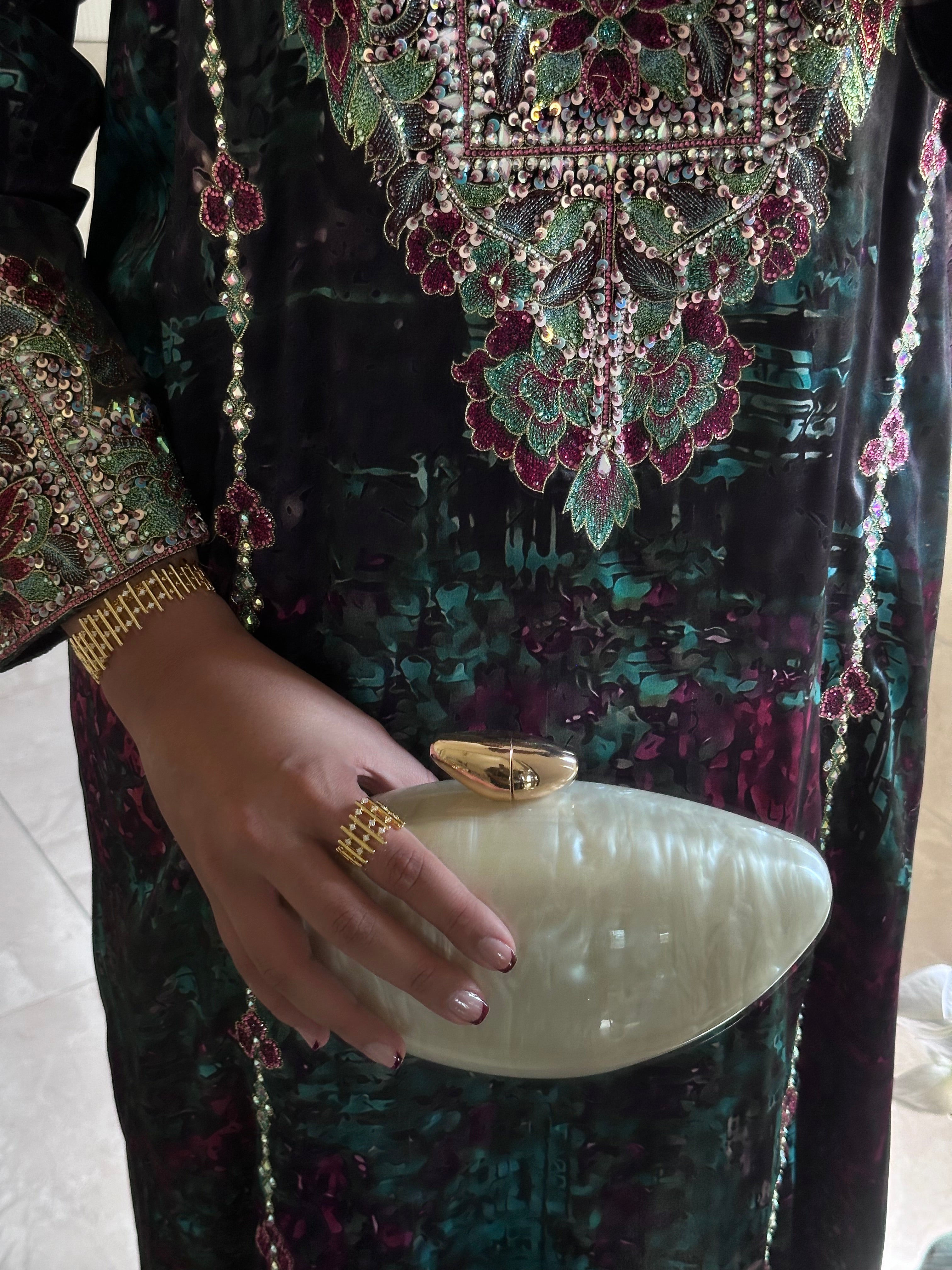 Decorative dress with intricate patterns and a hand holding a white clutch.