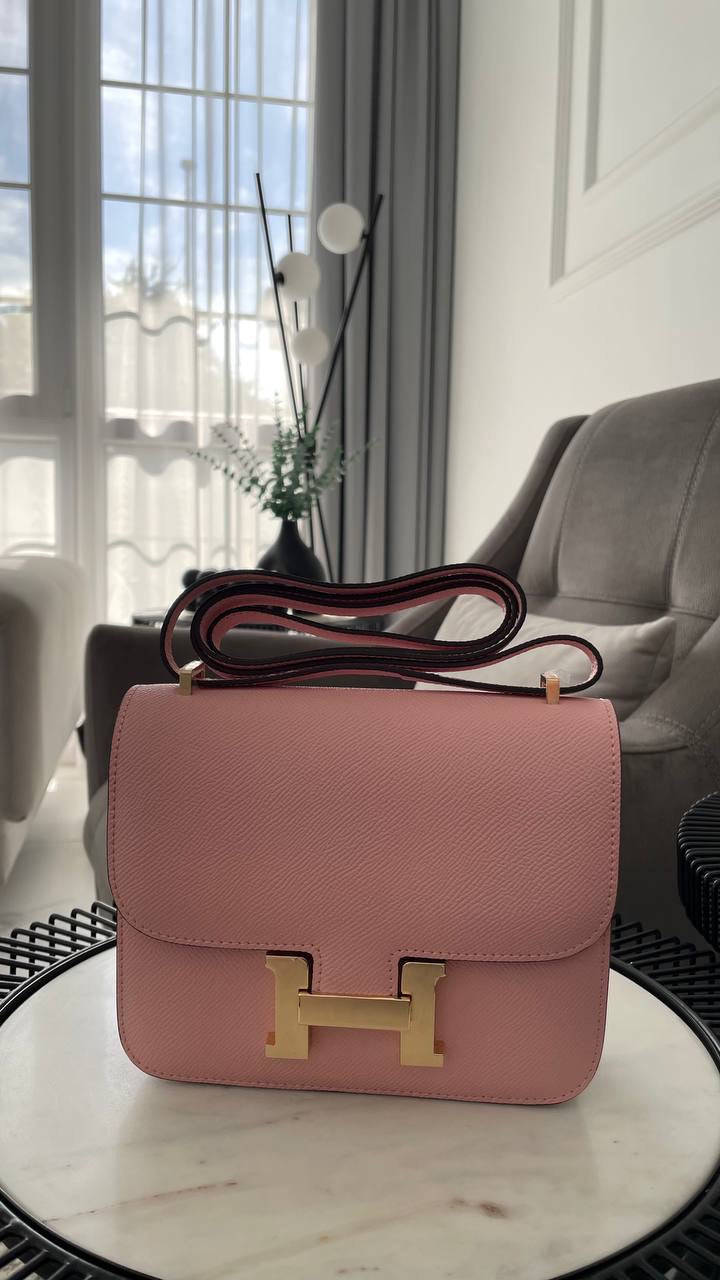 Pink handbag with gold hardware on a marble surface in a room with a couch and window.