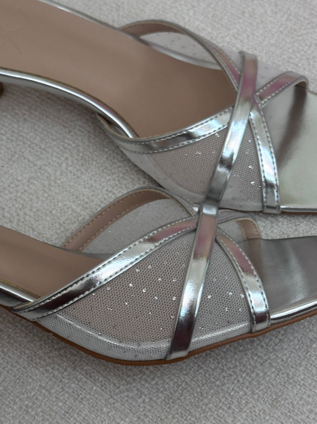 Silver high-heeled shoe with criss-cross straps on a neutral background