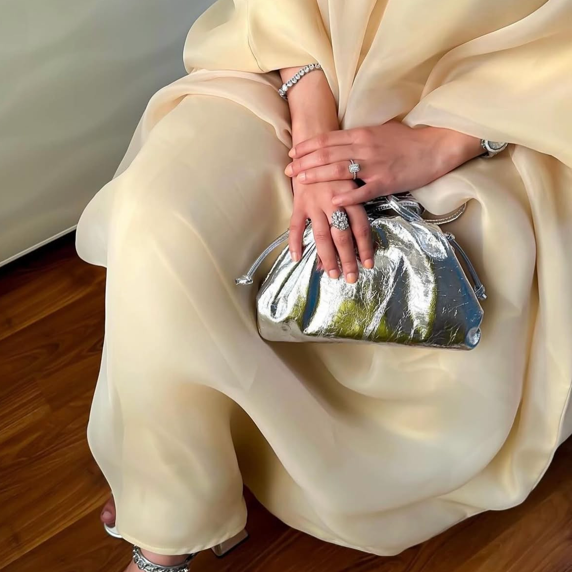 Person holding a silver clutch bag in a minimalistic setting