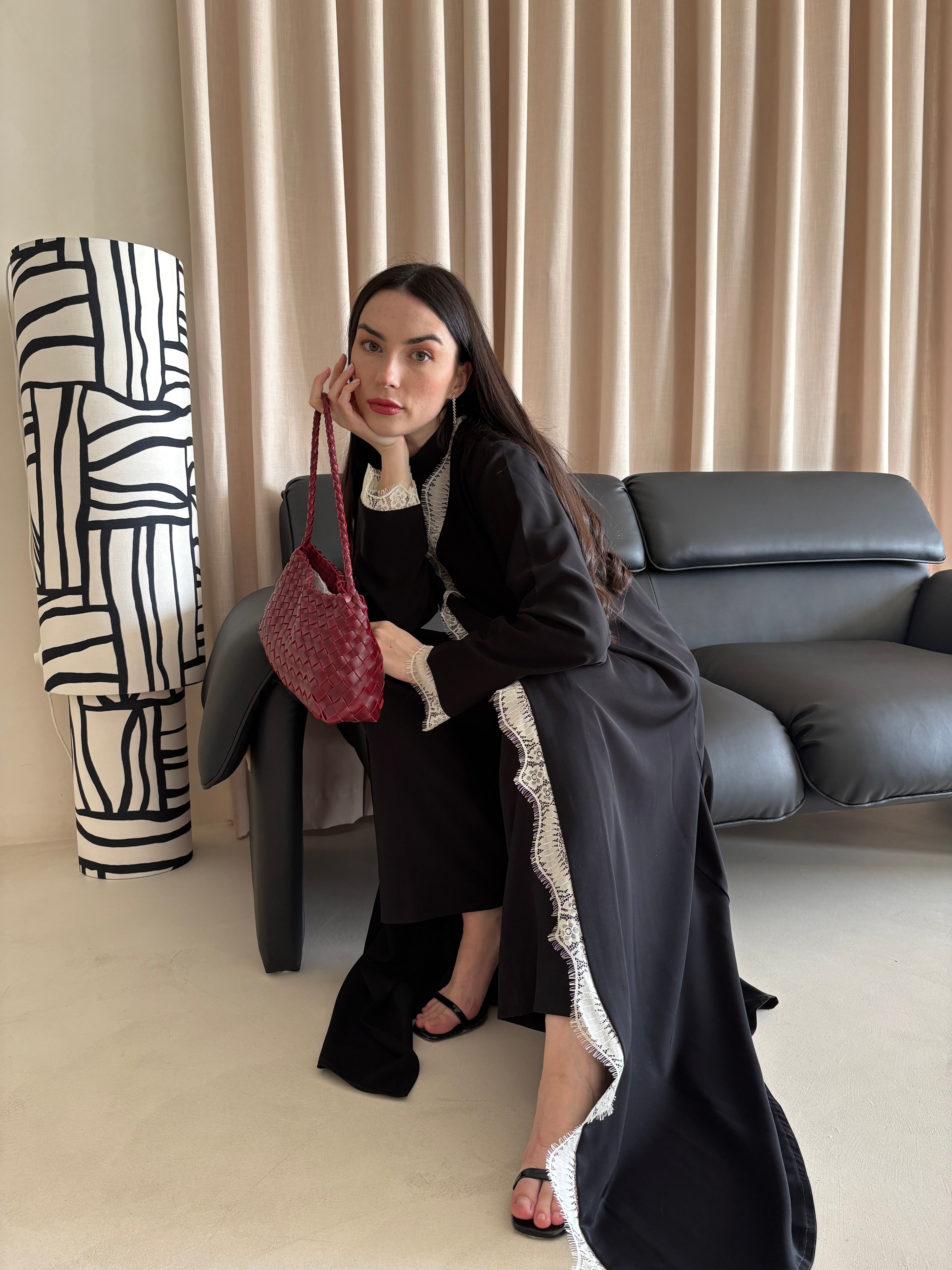 Woman in a black outfit with white trim holding a red handbag in a living room.