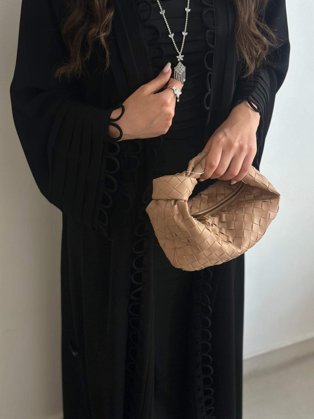 Person holding a beige woven handbag against a plain background