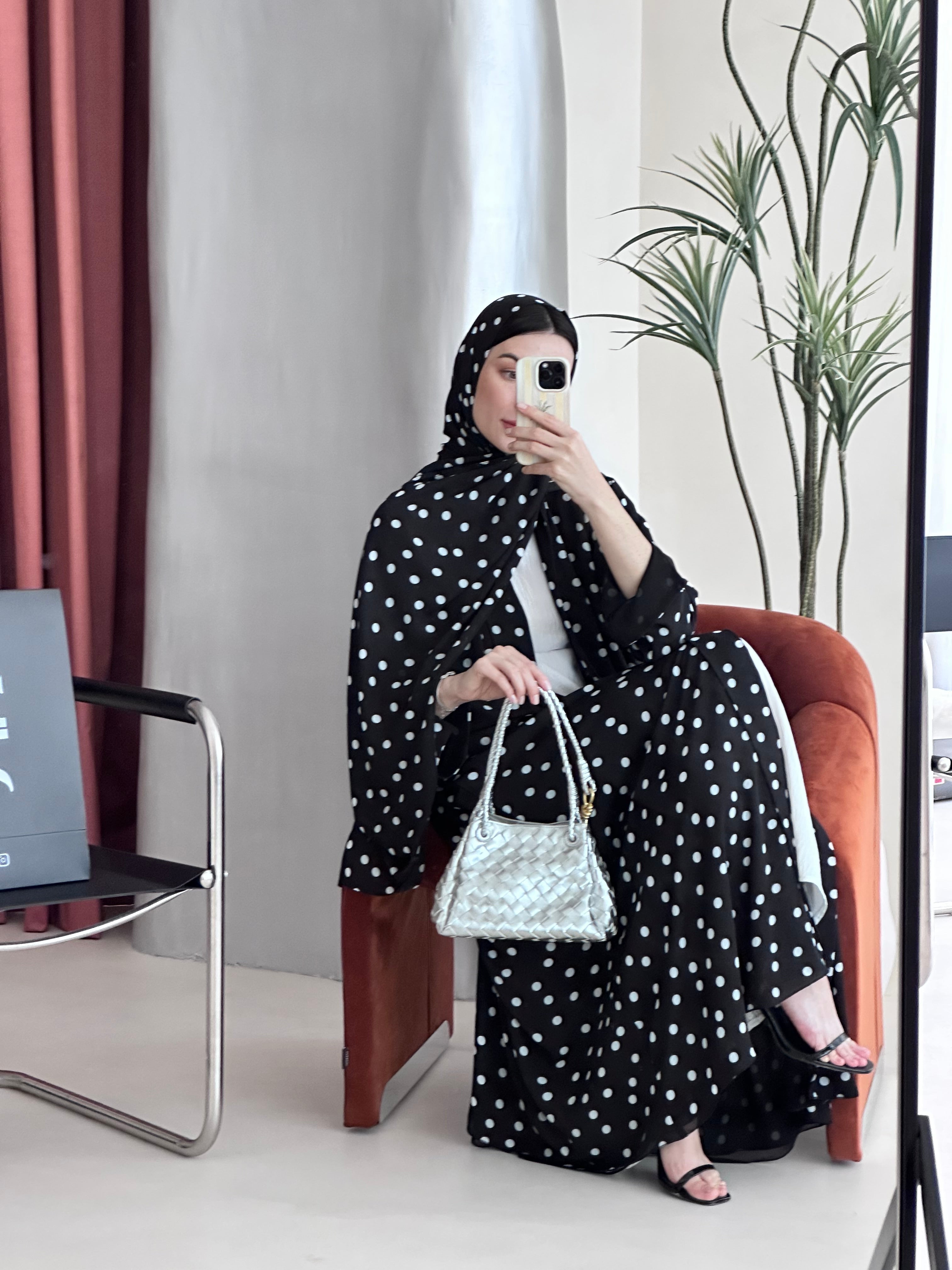 Woman in a black polka dot dress sitting on a bench with a white handbag.