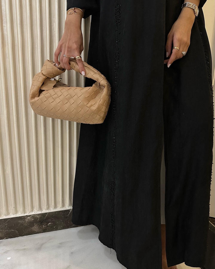 Person holding a beige woven handbag against a neutral background