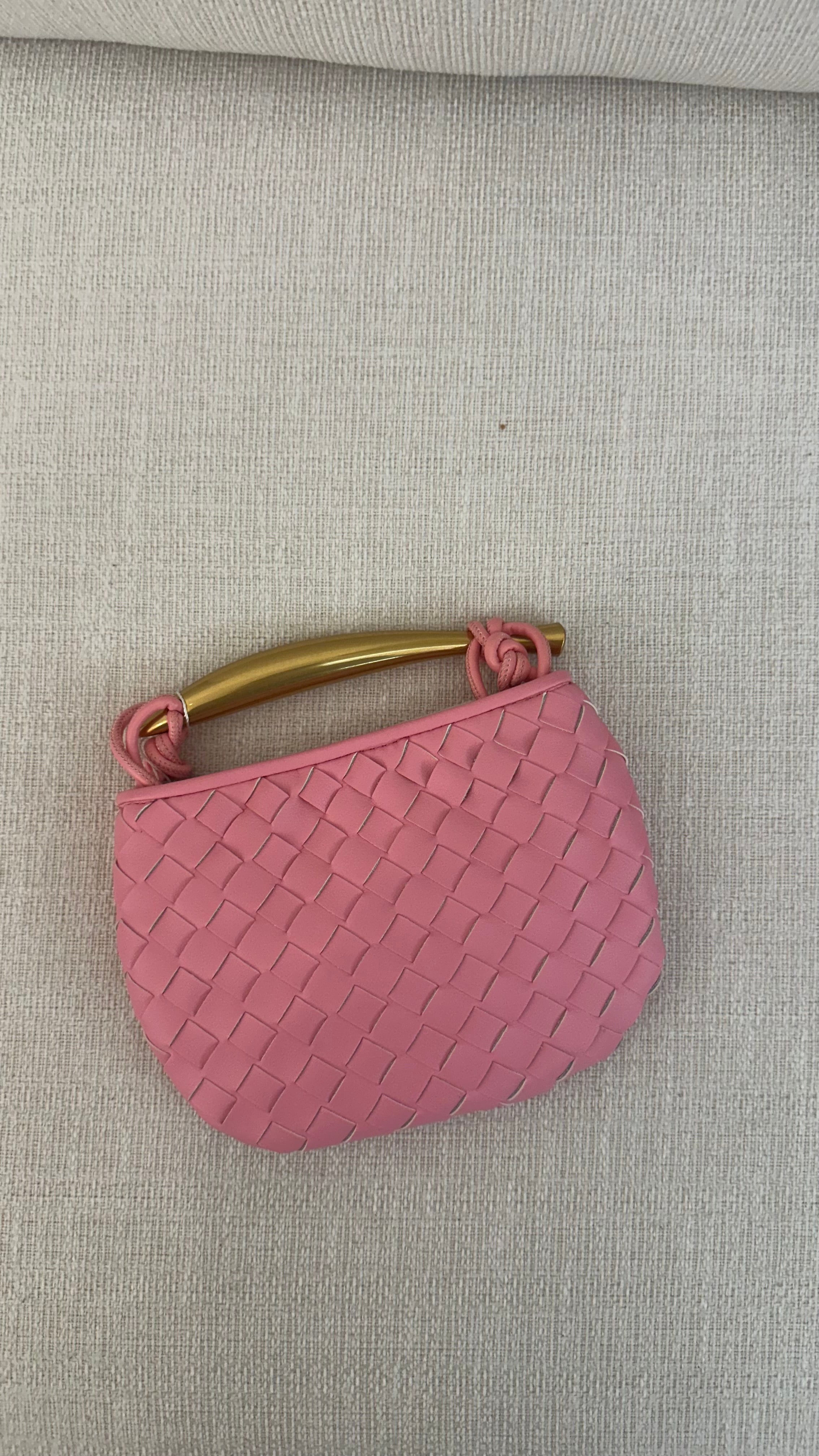 A pink mini bag with a textured surface and a gold-colored handle, displayed against a neutral background.