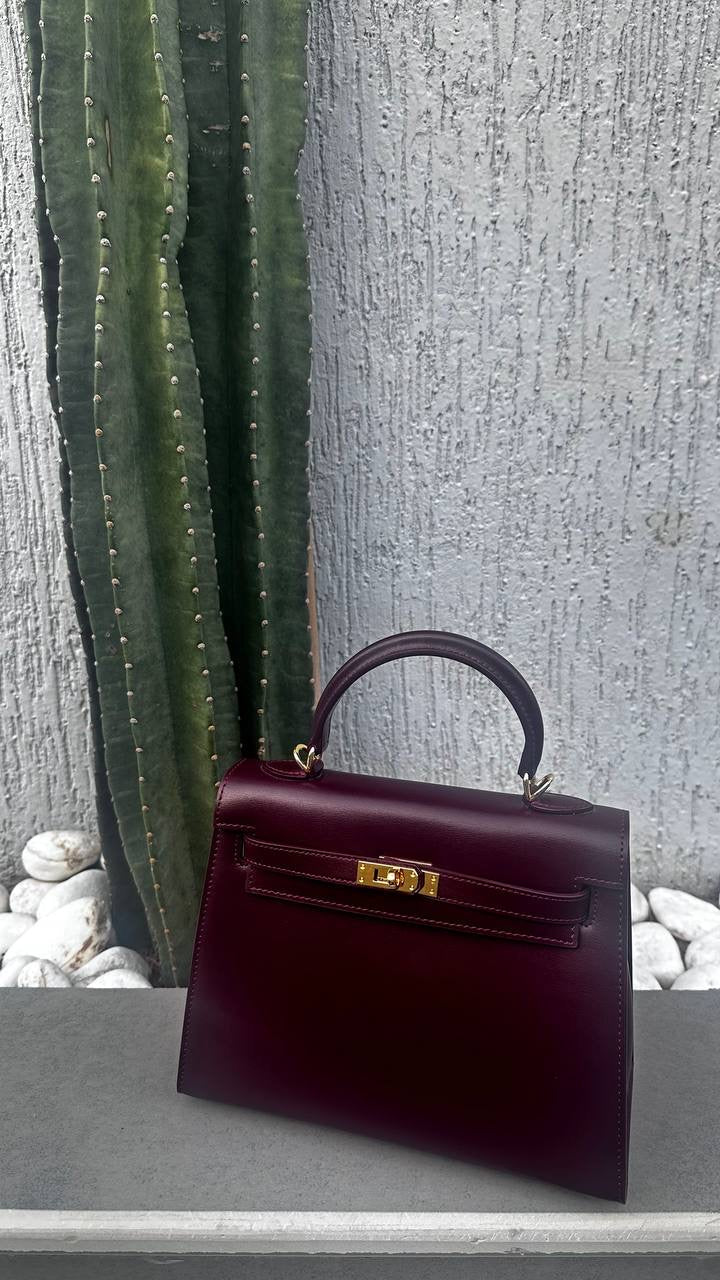 Burgundy handbag with gold hardware on a stone surface against a textured wall.