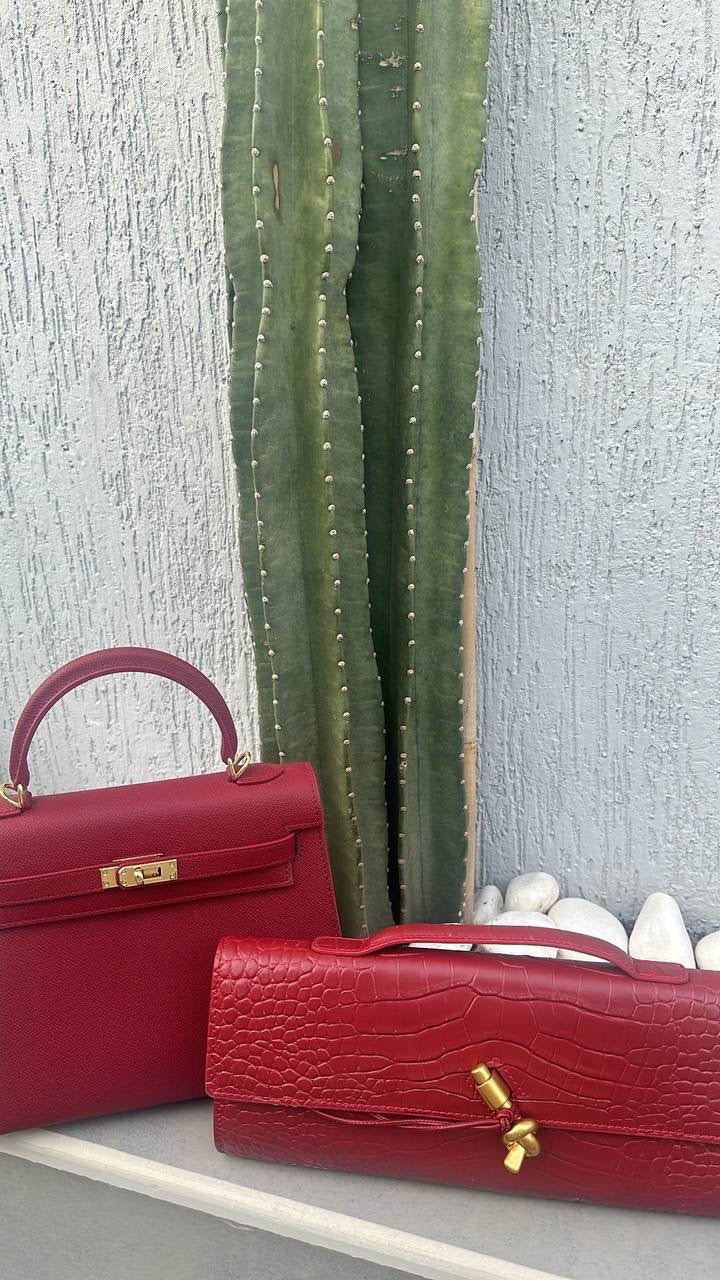 Two red handbags with gold hardware on a light gray surface with a textured wall background.