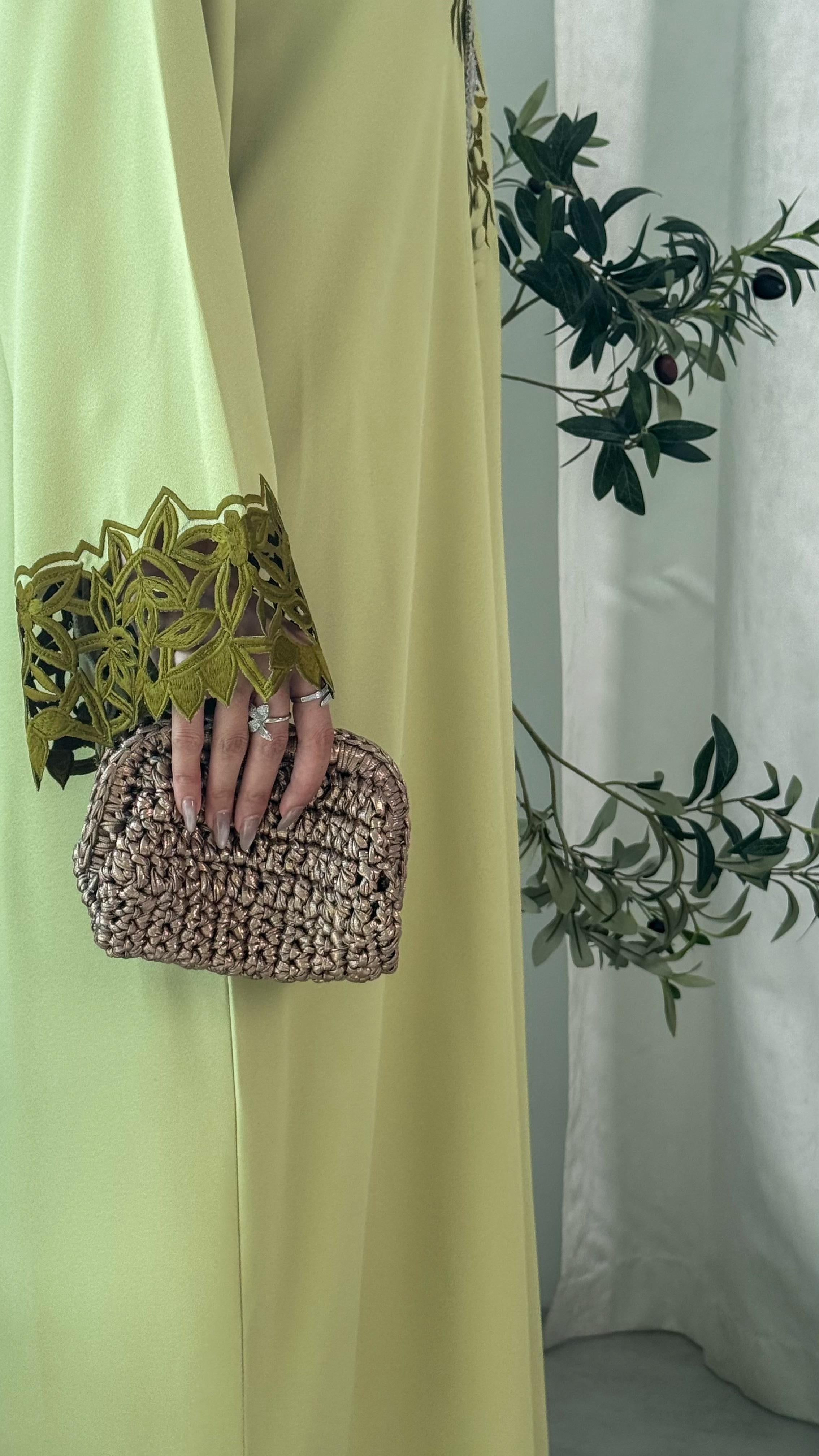 Person holding a woven clutch with a light green dress and white curtain background
