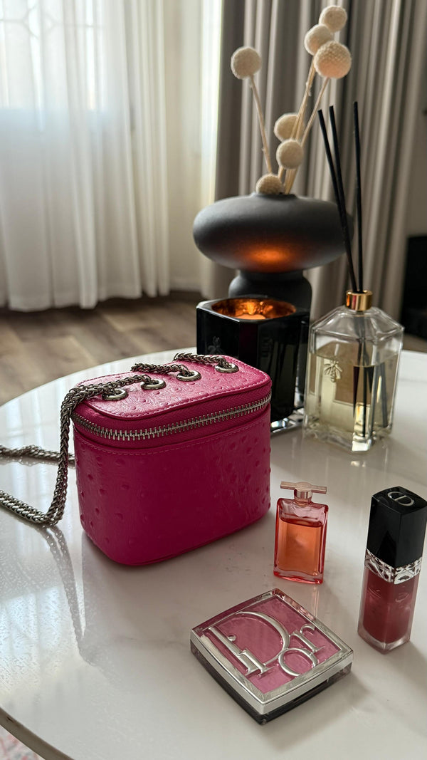 Pink handbag, perfume bottles, and a compact mirror on a table with a blurred background