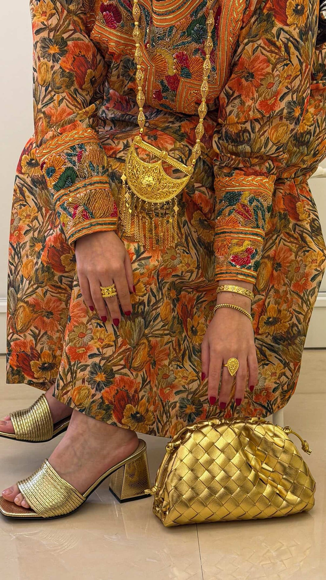 Person wearing a floral dress with gold accessories including a handbag and rings.