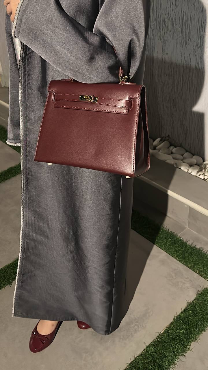 Person holding a brown leather handbag on a grassy area.