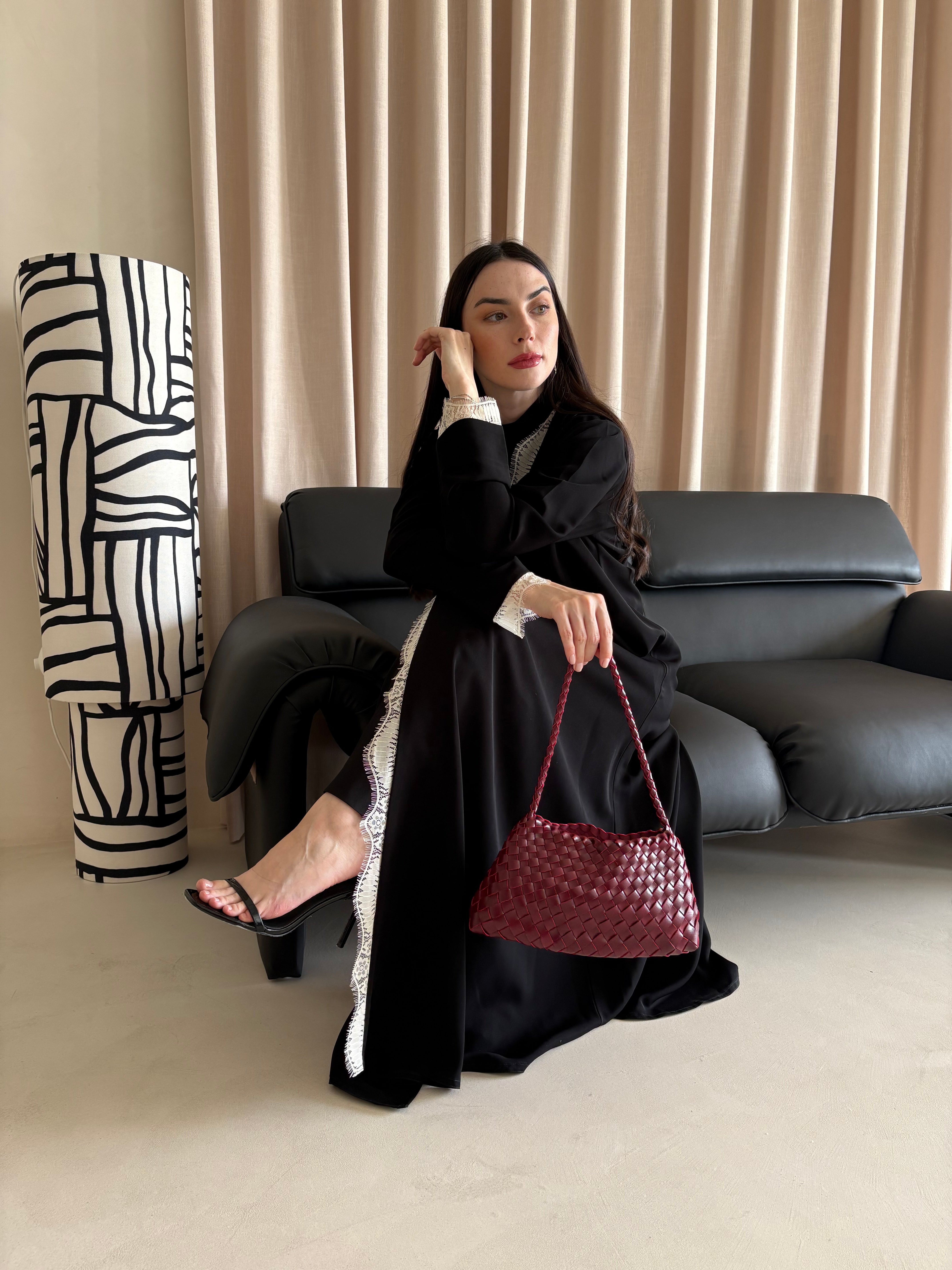 Woman in a black outfit holding a red handbag in a room with a black sofa and abstract sculpture.