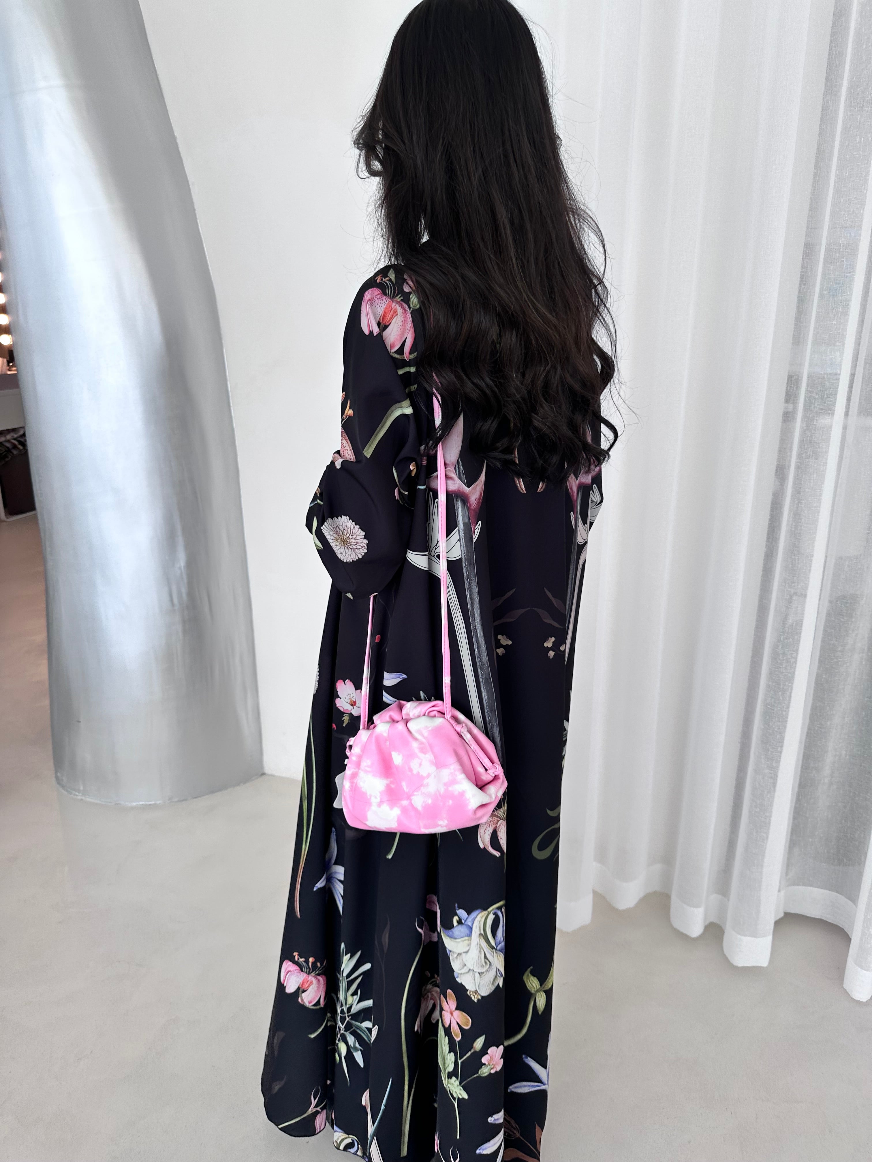Woman wearing a floral dress with a pink bag against a white curtain background