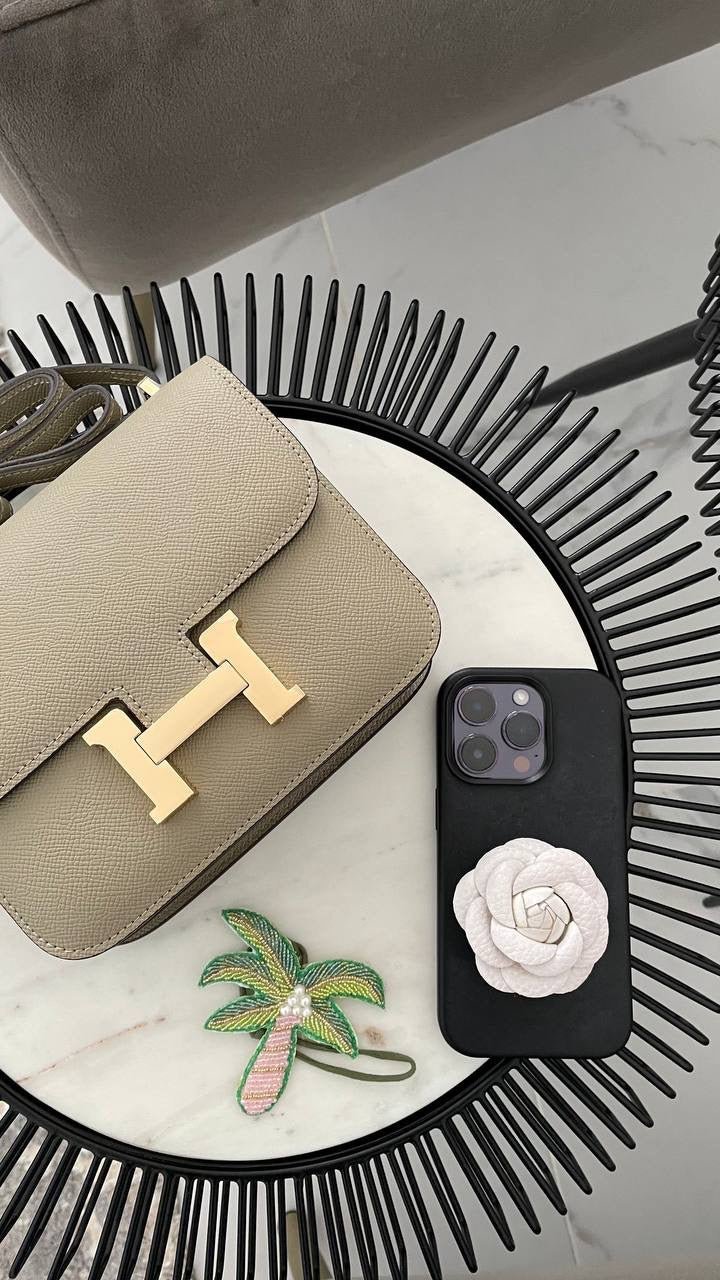 A gray handbag with gold hardware placed on a table next to a smartphone with a black case and a decorative item.