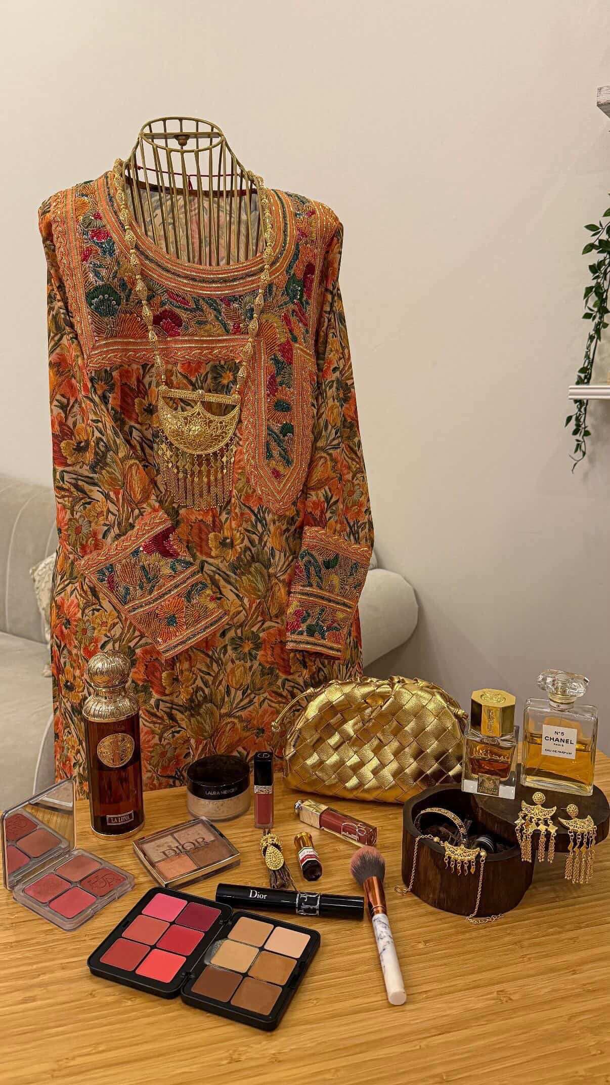 Makeup products and a patterned top on a wooden surface with a neutral background