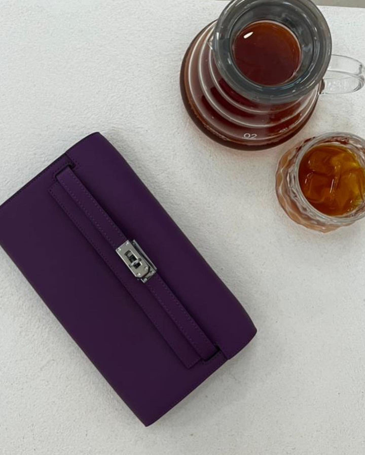 Purple clutch bag on a light gray surface with two glass jars containing a amber-colored liquid.