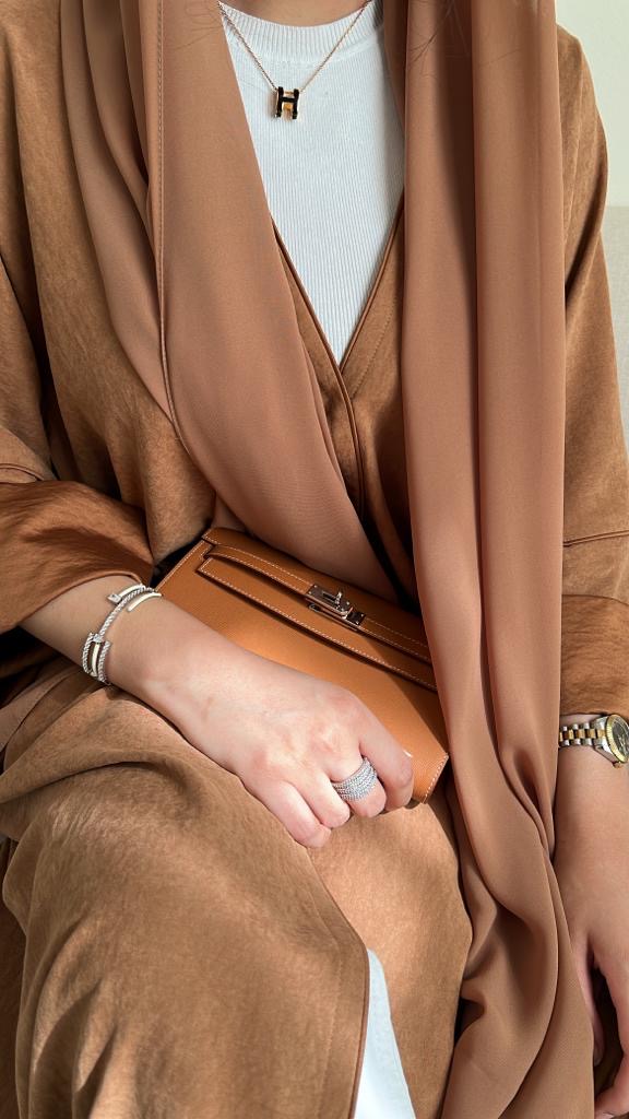 Person wearing a brown coat with a white shirt underneath, holding a brown handbag.
