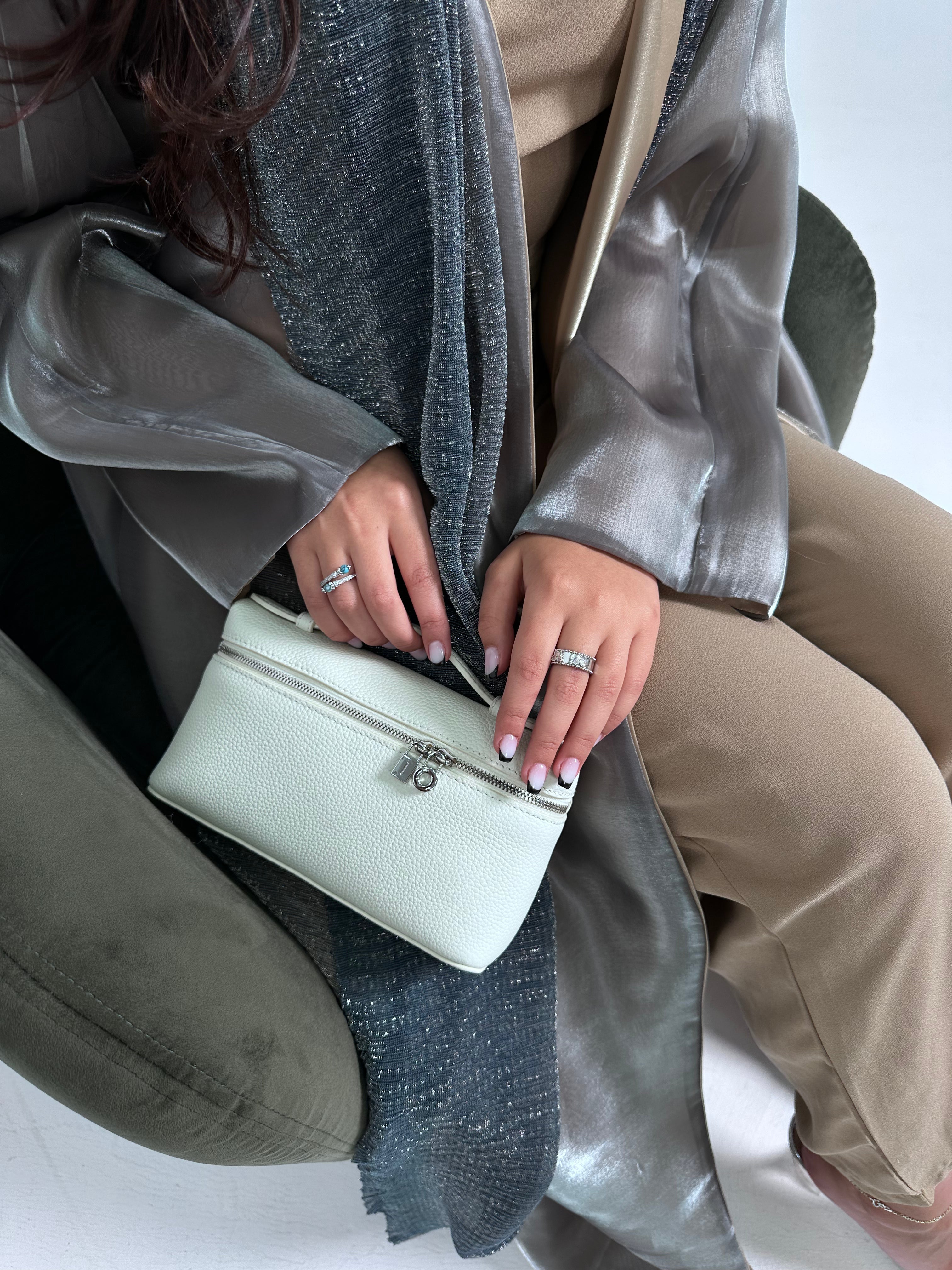 A person holding a white tote handbag with a long strap and a small lock detail on the front.
