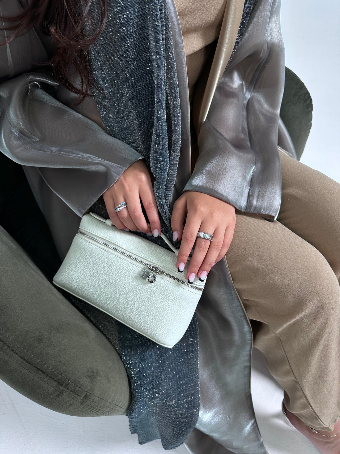 A person holding a white tote handbag with a long strap and a small lock detail on the front.