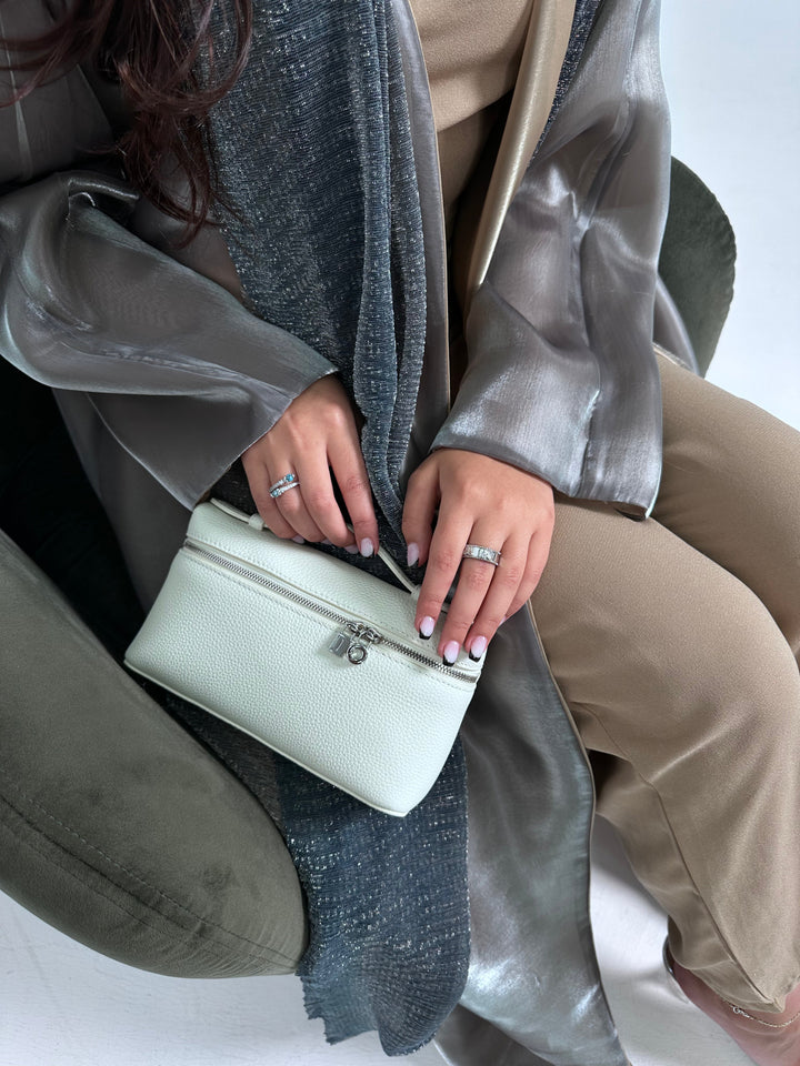 A person holding a white tote handbag with a long strap and a small lock detail on the front.