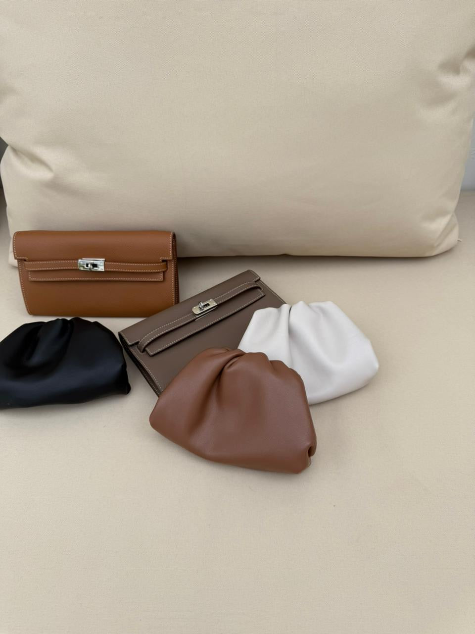 Five leather bags in different colors arranged on a beige surface.