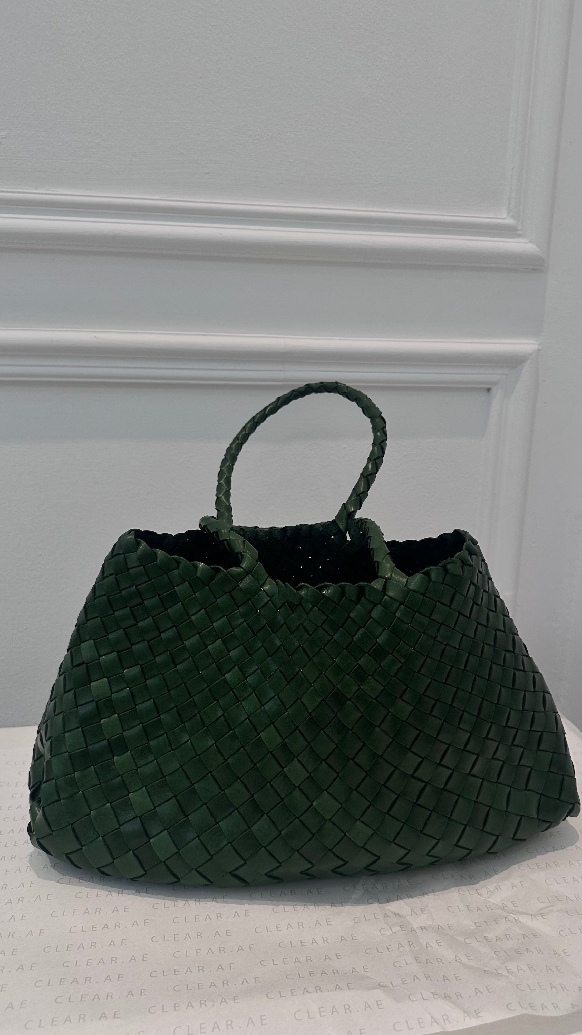 Green woven handbag on a white surface with a light gray background