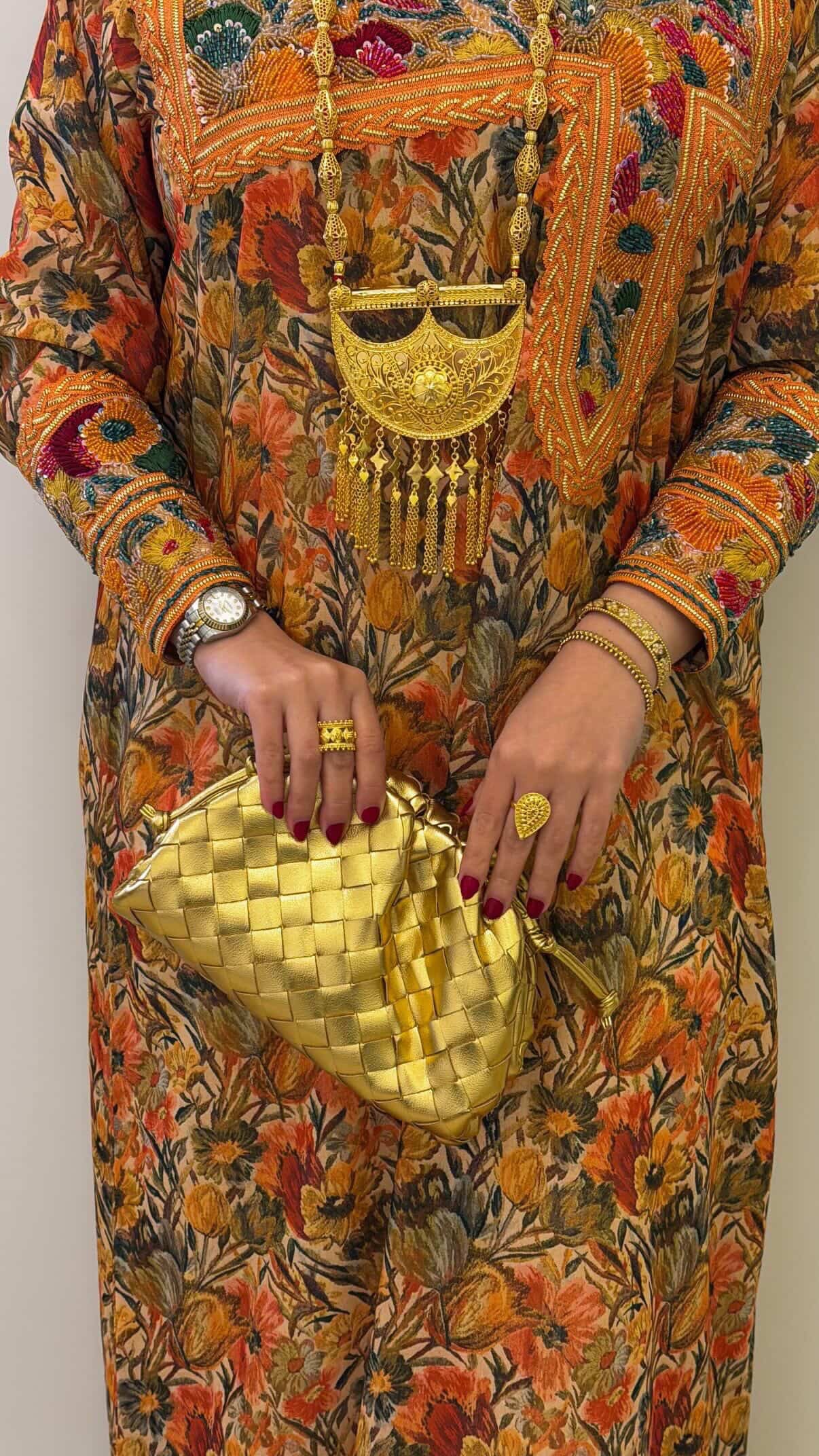 Person wearing a colorful traditional outfit with a gold clutch