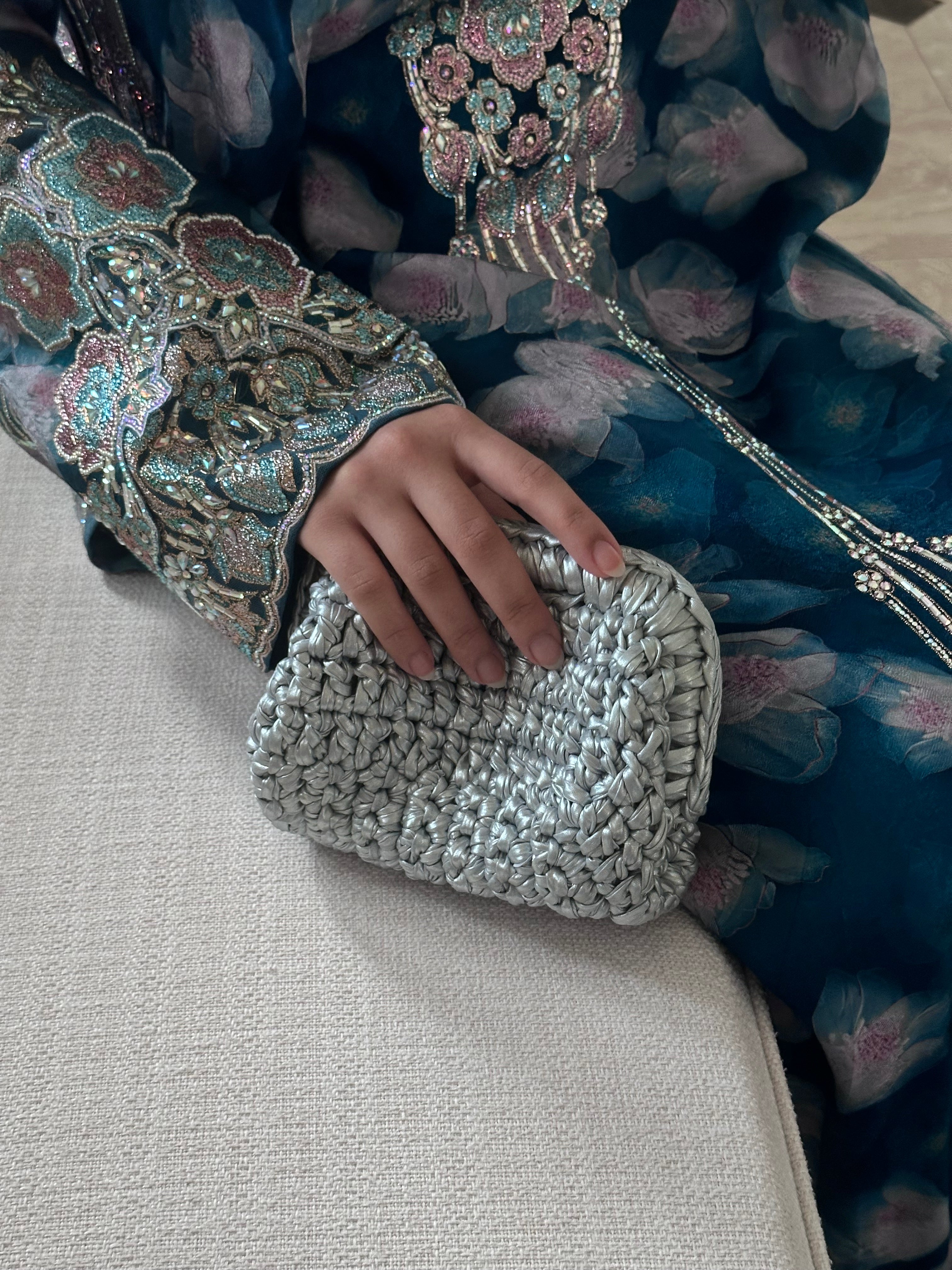 Hand holding a silver clutch with embroidered traditional outfit in the background