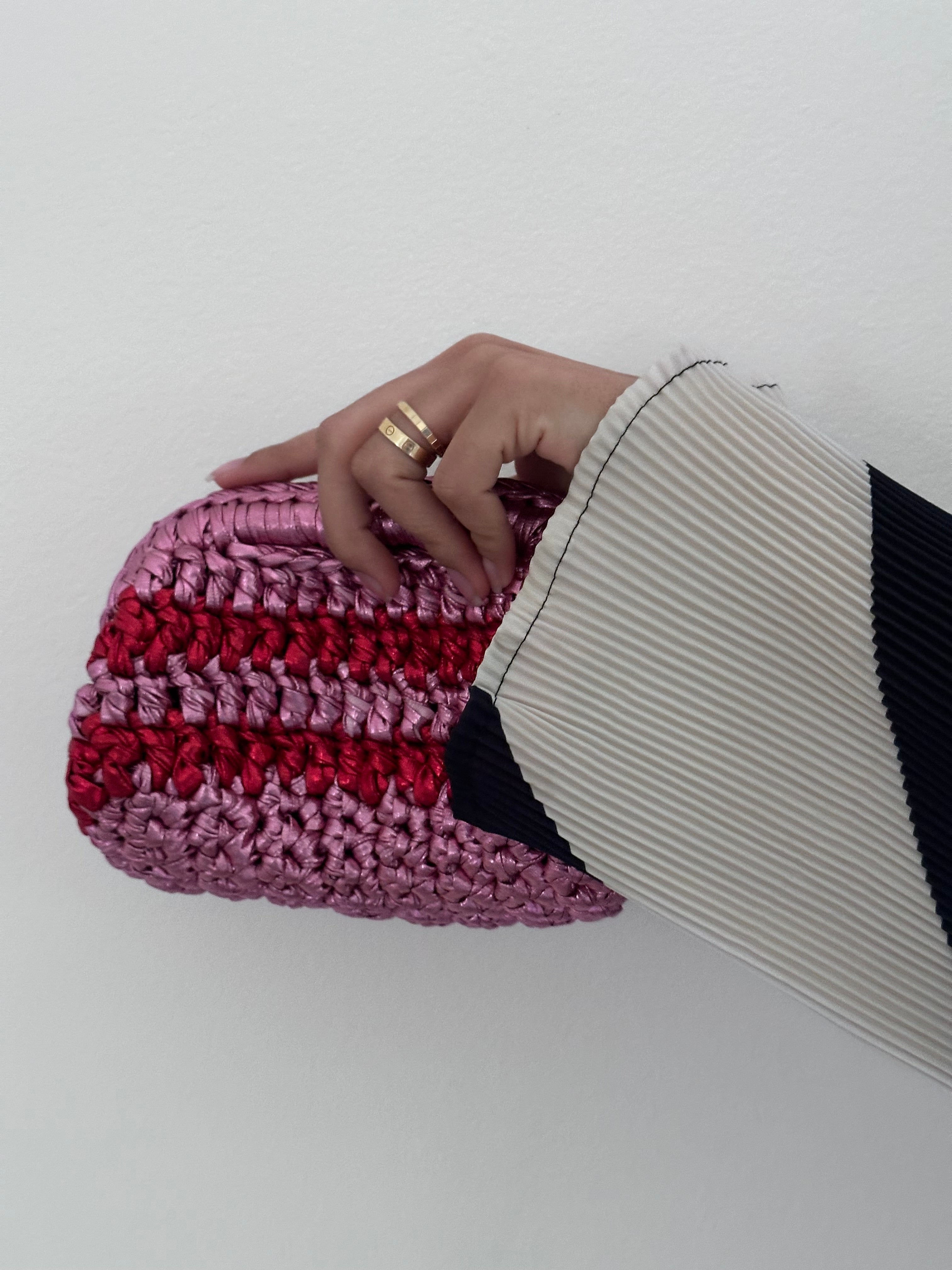 Hand holding a pink and red striped clutch bag against a white background