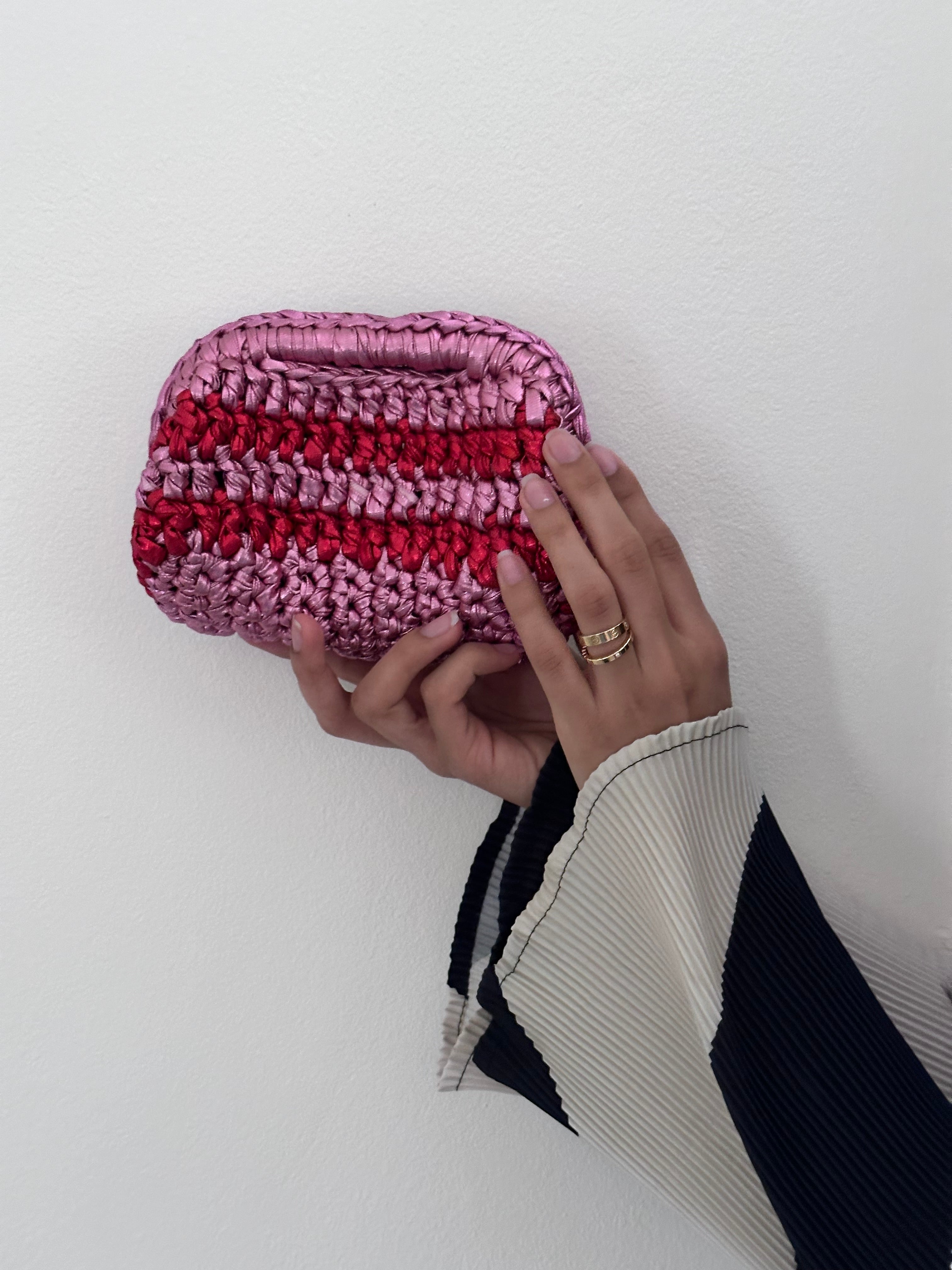 Hand holding a pink and red striped clutch bag against a white background