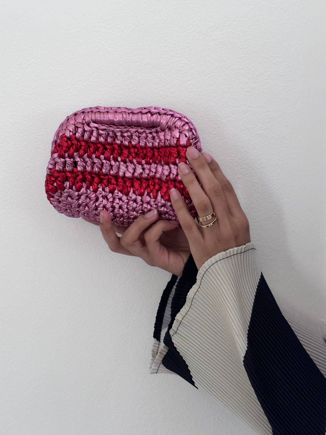 Hand holding a pink and red striped clutch bag against a white background