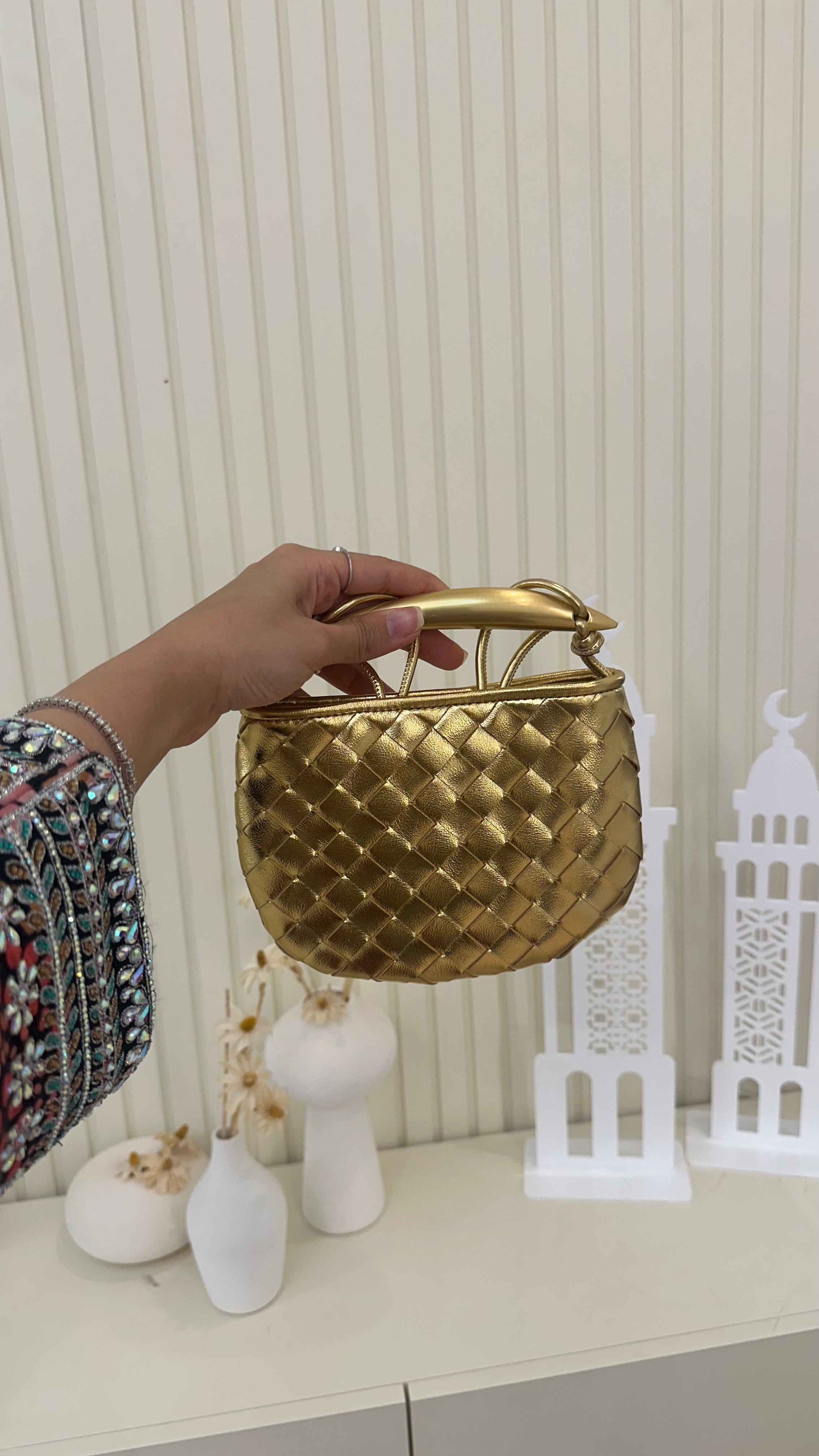 A person holding a gold-colored, quilted handbag with a metal handle.