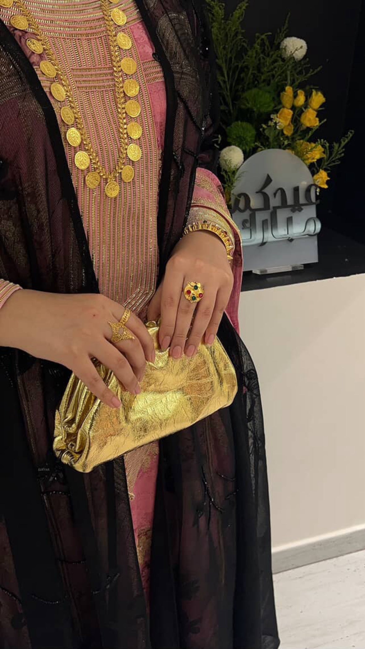 Person holding a gold clutch with traditional attire and jewelry in the background