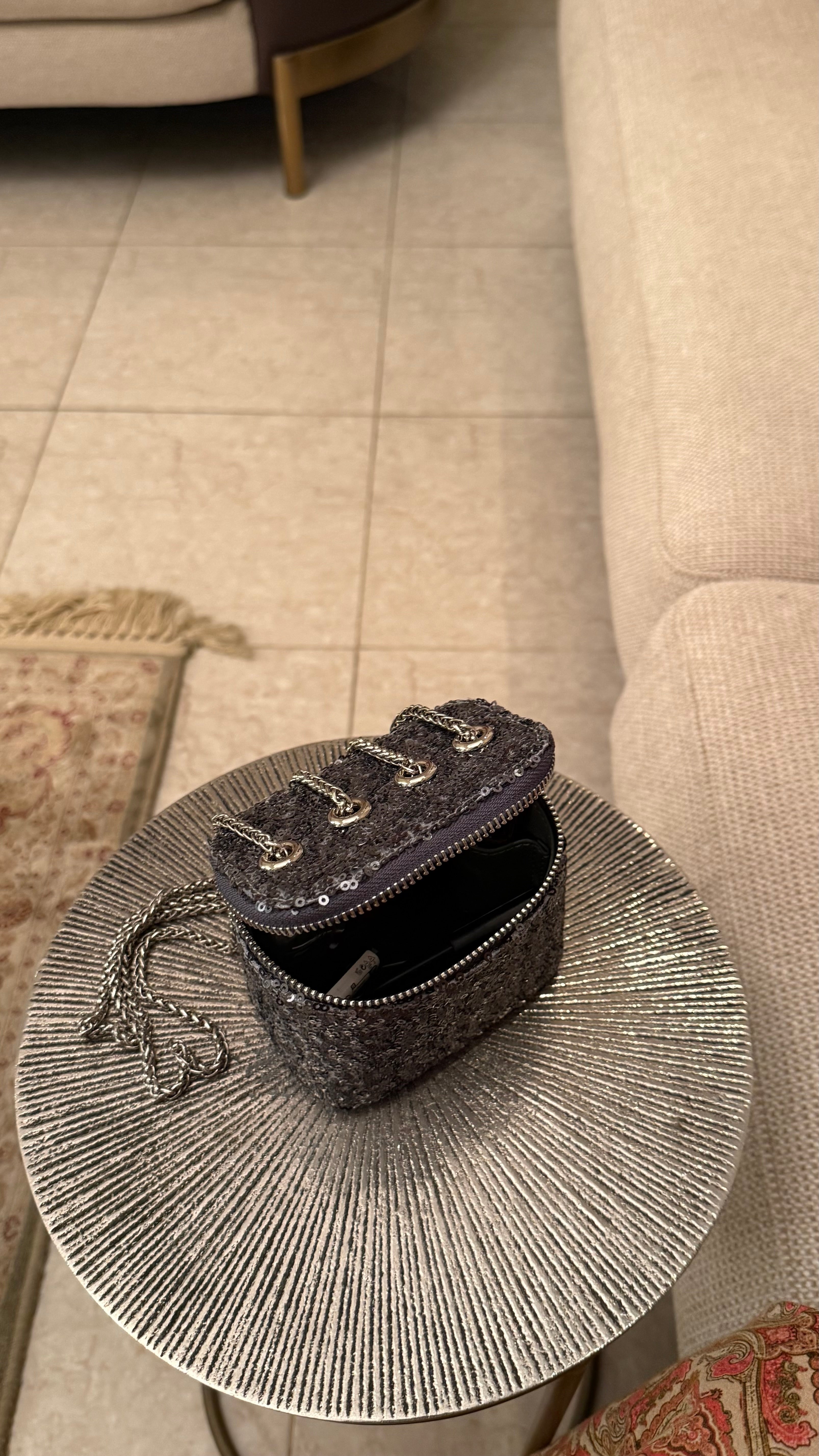 Small black handbag on a round, textured side table next to a beige sofa.
