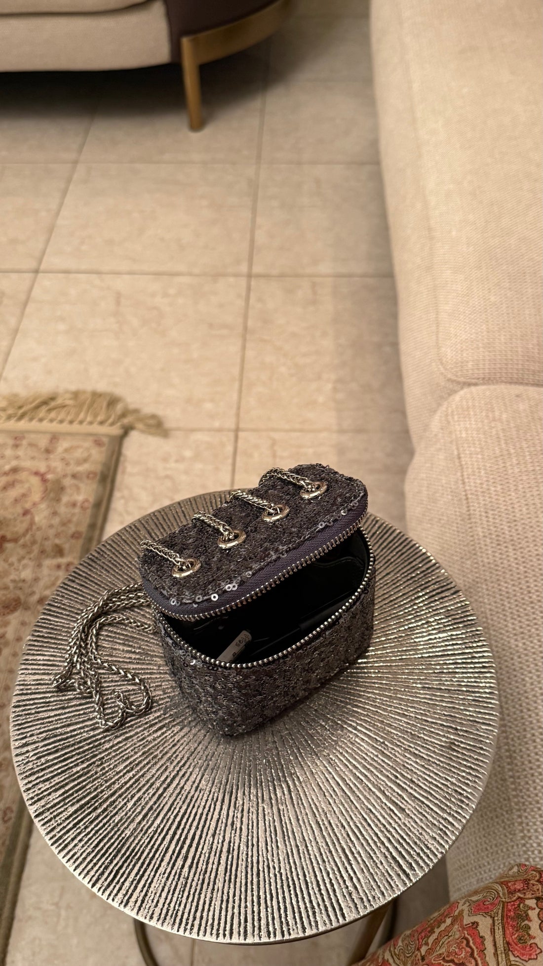 Small black handbag on a round, textured side table next to a beige sofa.