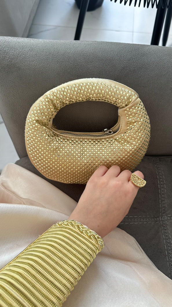 A person sitting with a gold-colored, textured handbag in their lap.