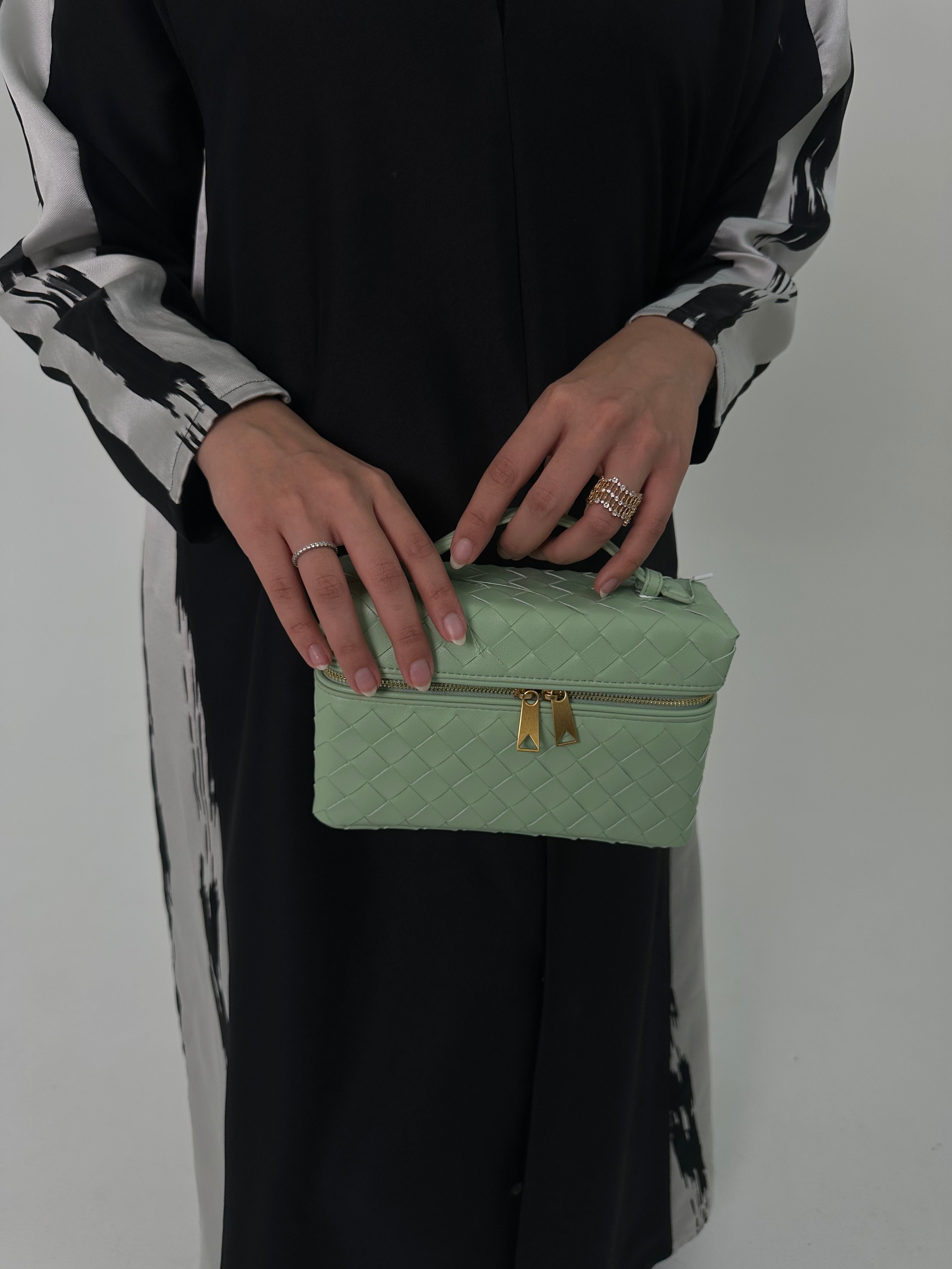 A person holding a light green quilted leather medium bag with a zipper and a long adjustable strap.