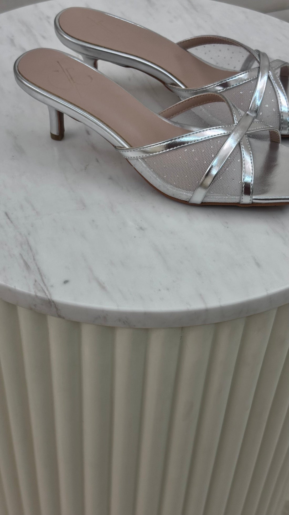 Silver high-heeled sandals on a marble surface