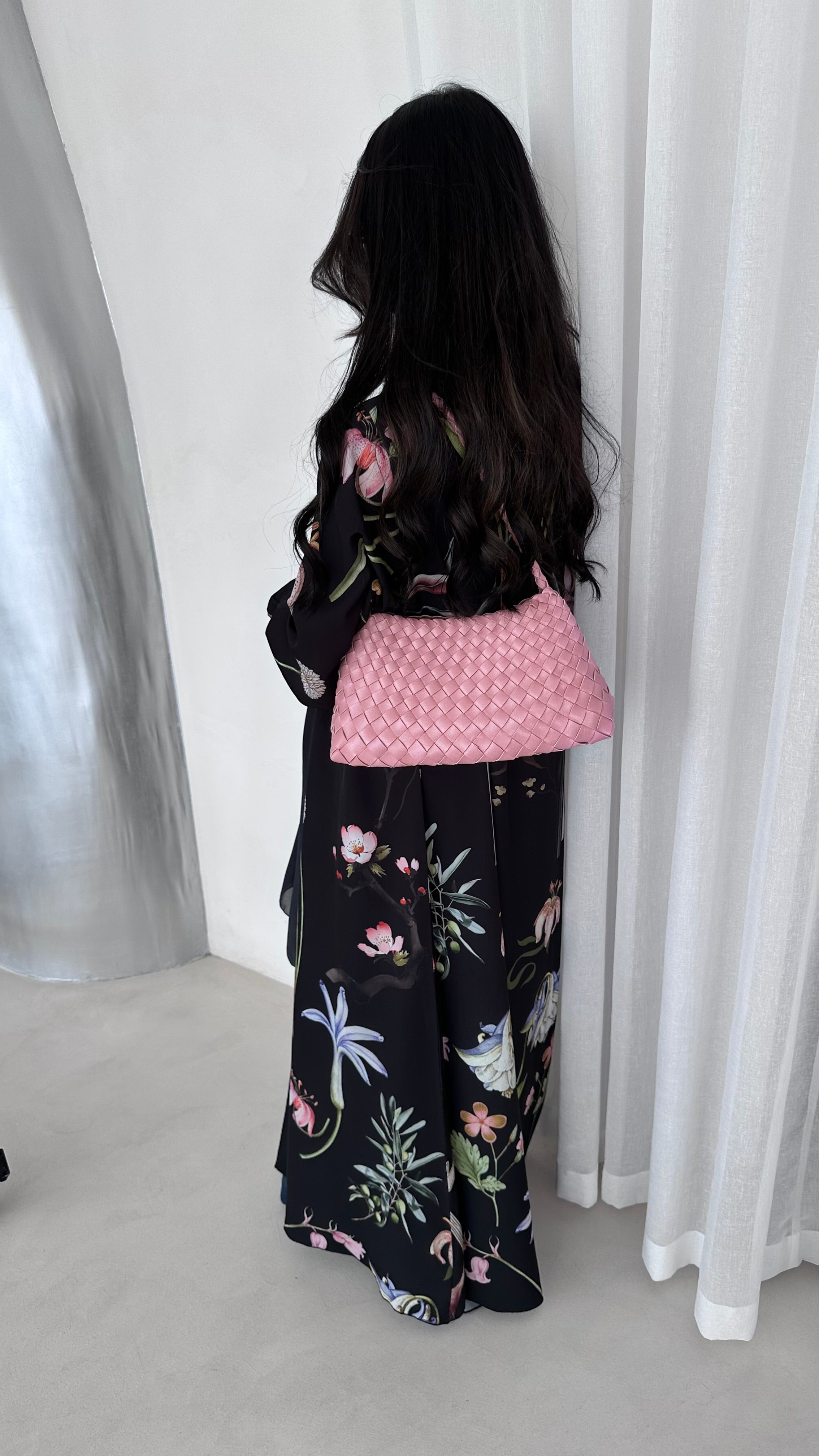 Person wearing a black floral outfit with a pink top against a white curtain background