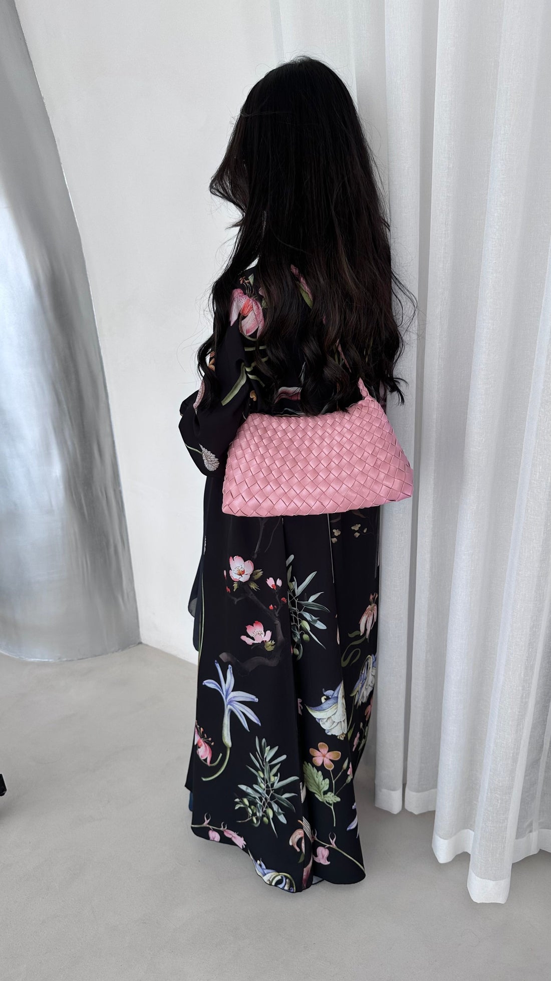 Person wearing a black floral outfit with a pink top against a white curtain background