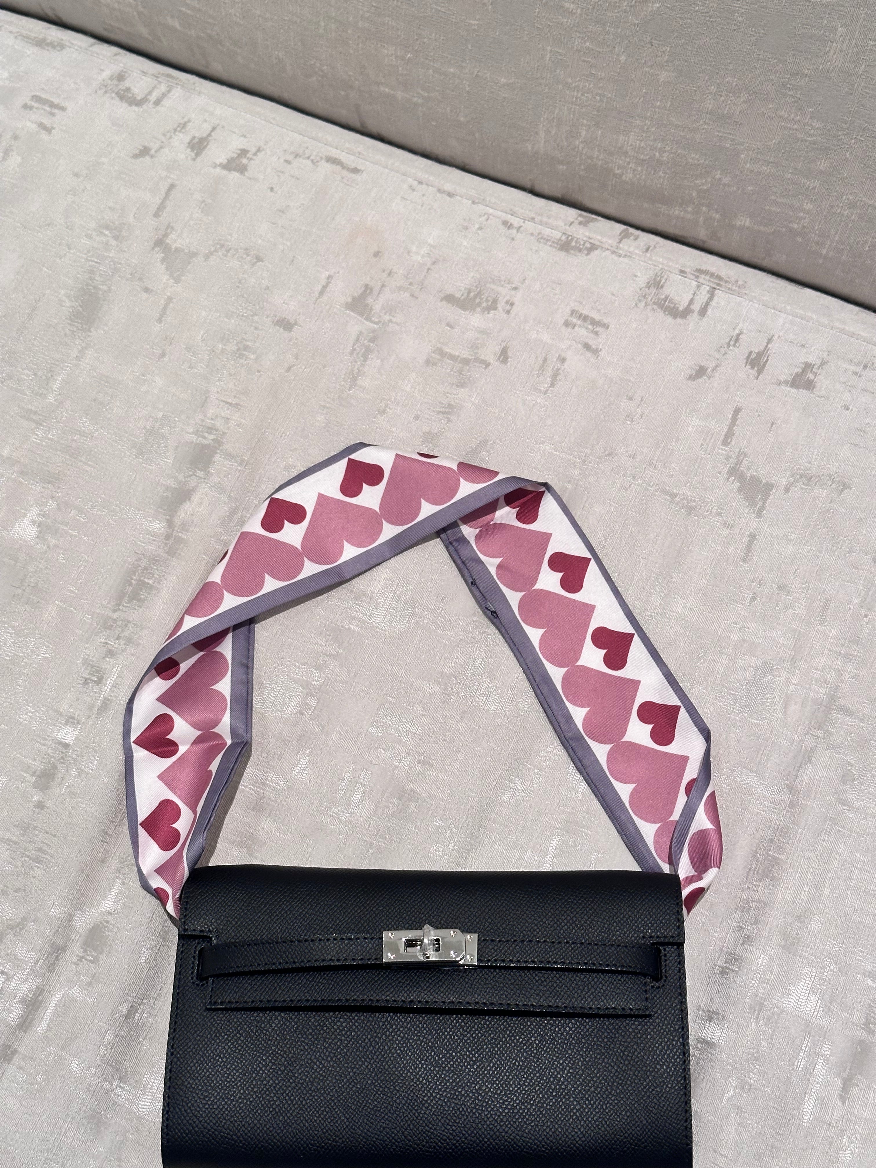Black handbag with a pink heart-patterned strap on a gray surface
