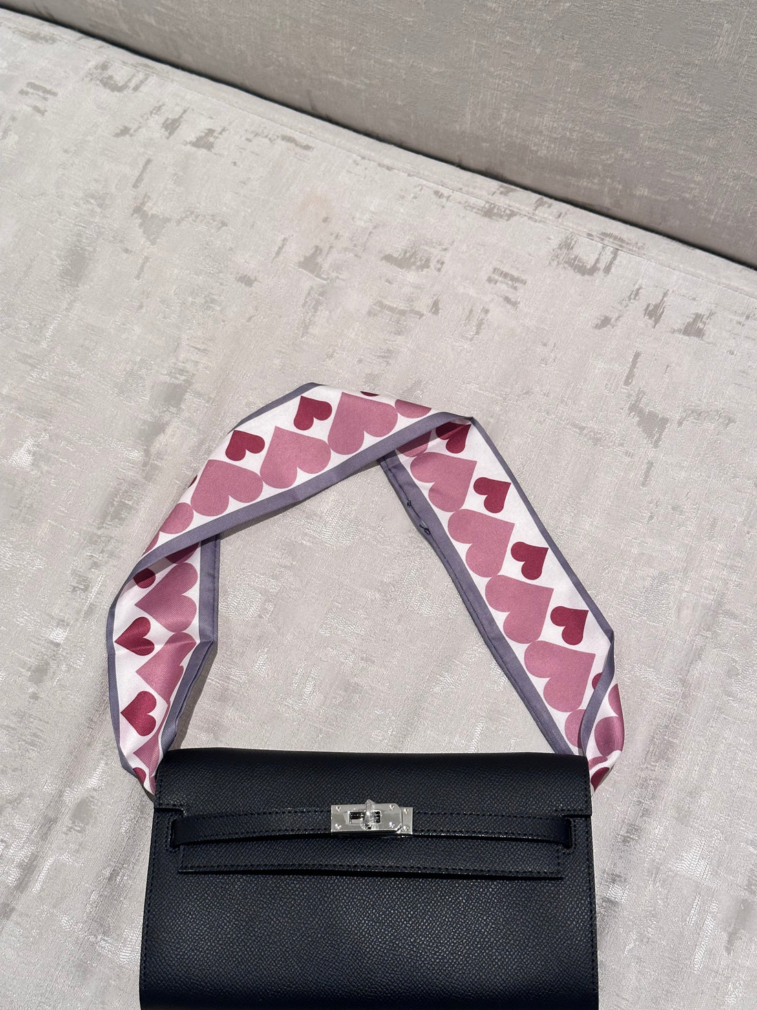 Black handbag with a pink heart-patterned strap on a gray surface